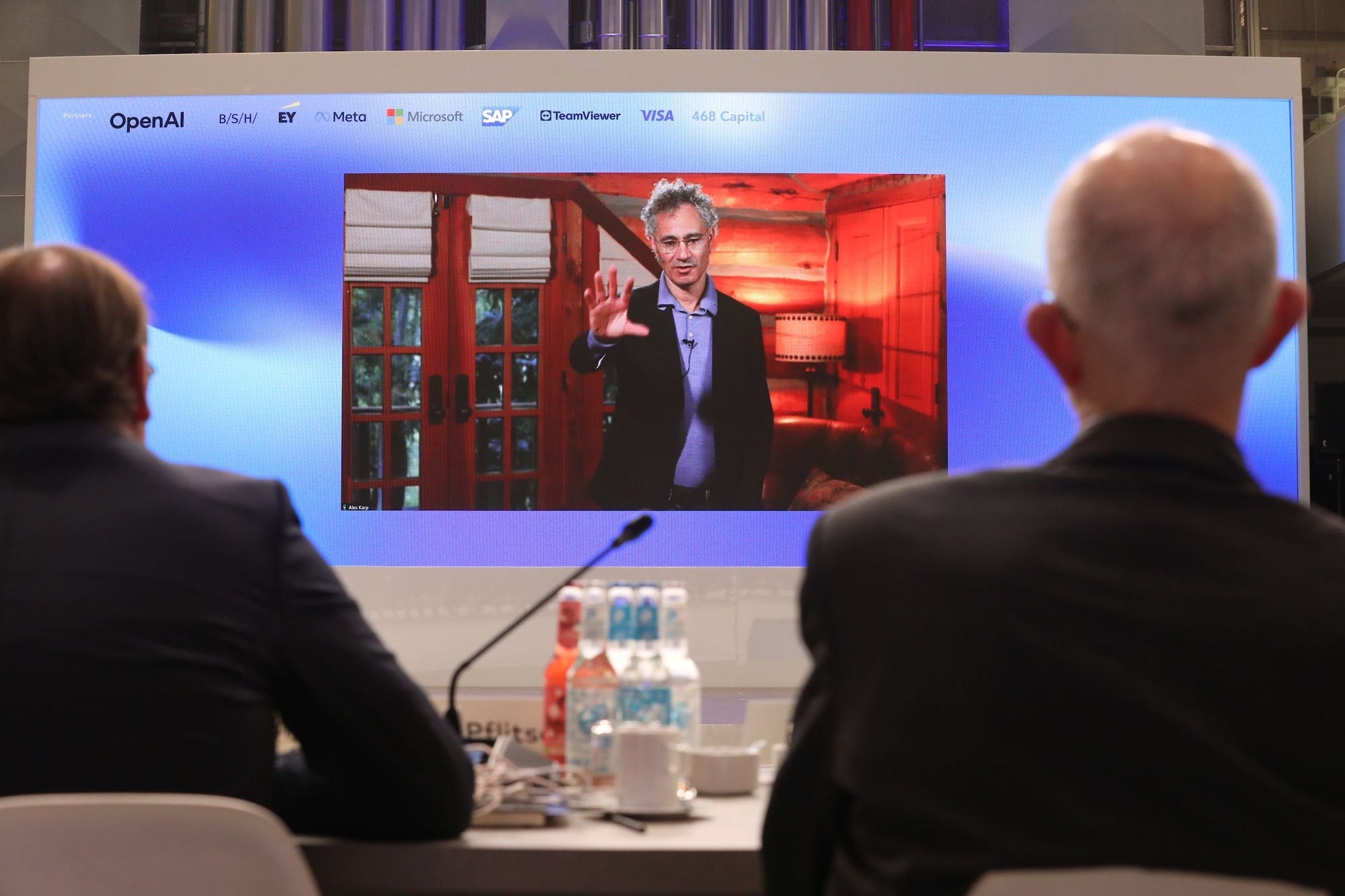 Palantir's Alex Karp is shown on a screen.