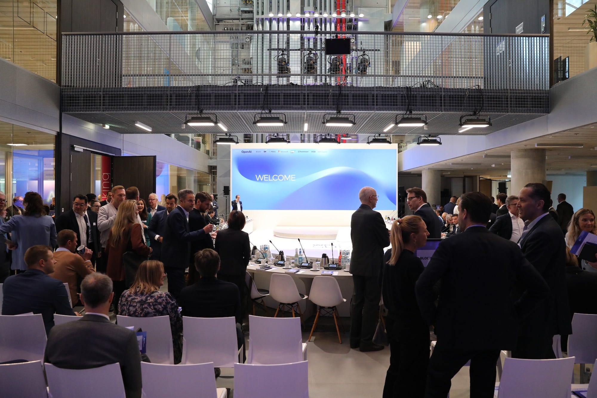 Professionals stand and talk amongst themselves around a conference table.