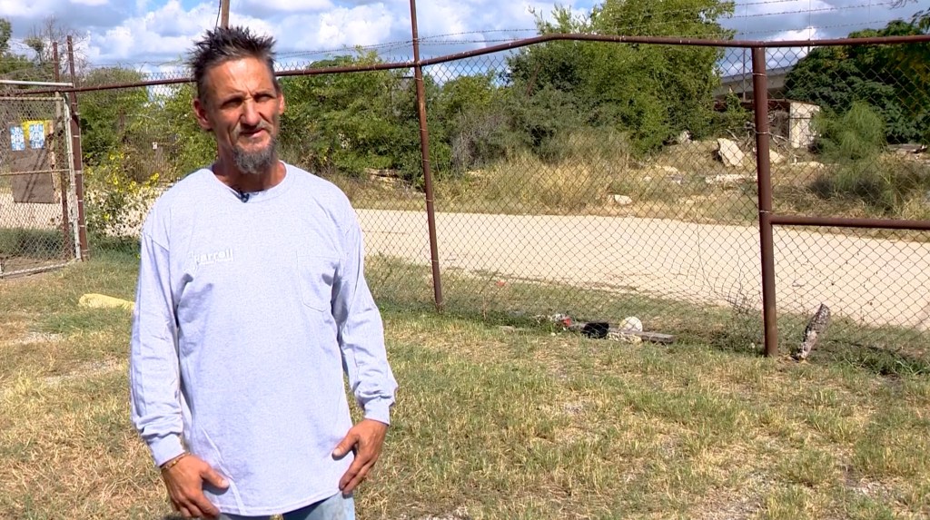 A plumber, Walter Stephens, stands outside near a chain link fence where he found a human skull.