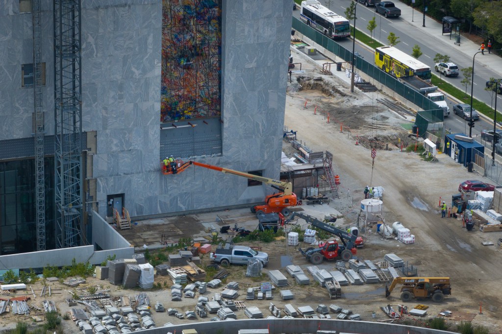 Aerial view of construction underway at the Obama Presidential Center in Chicago, with a large building under construction and several workers using heavy machinery.