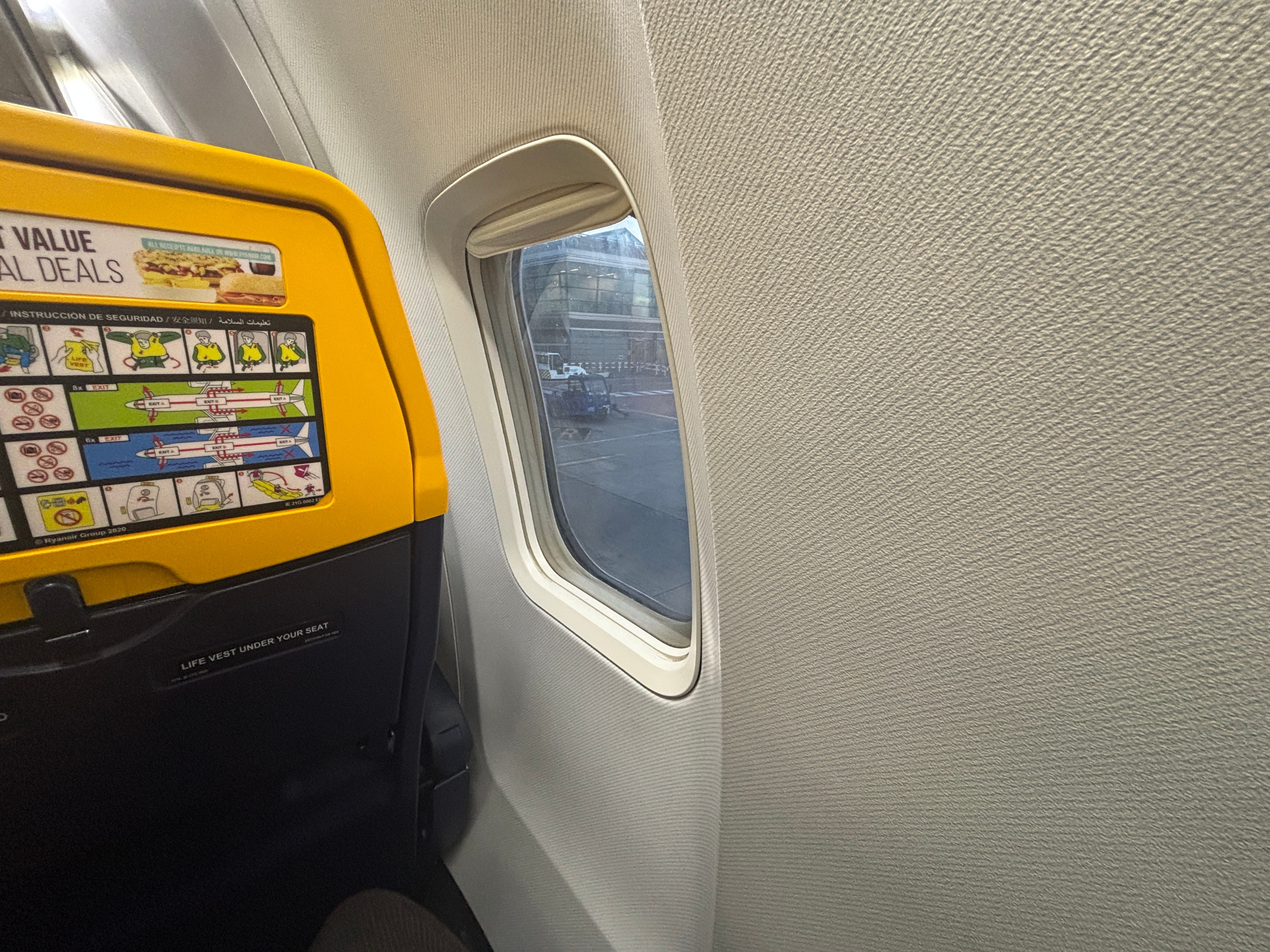 A first-person view from seat 12F on a Ryanair Boeing 737, with a window misaligned and a blank wall taking up much of the space.