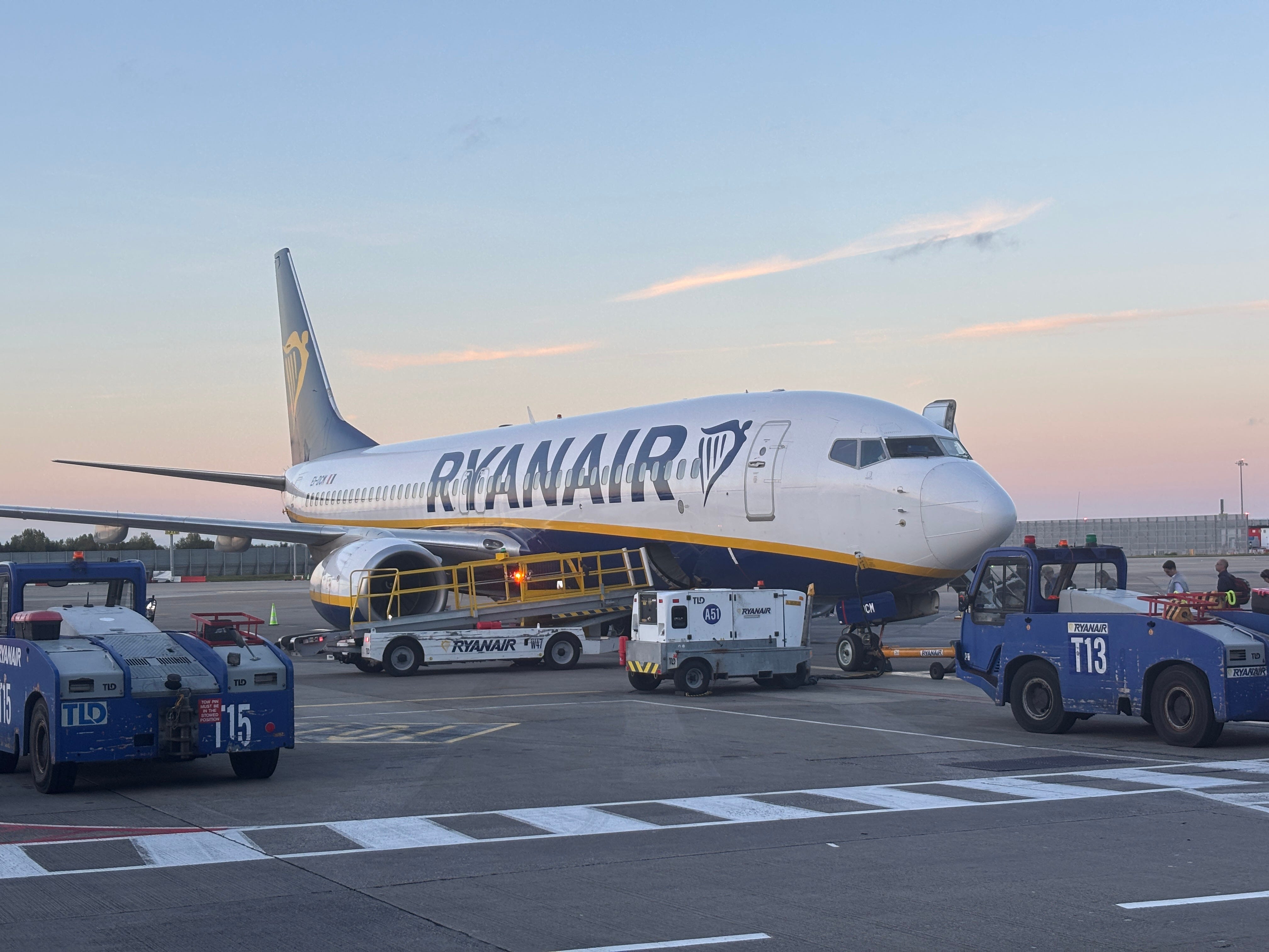 A Ryanair Boeing 737 parked at Dublin Airport during sunset, with ramp workers and airport vehicles attending to it, on September 23, 2025