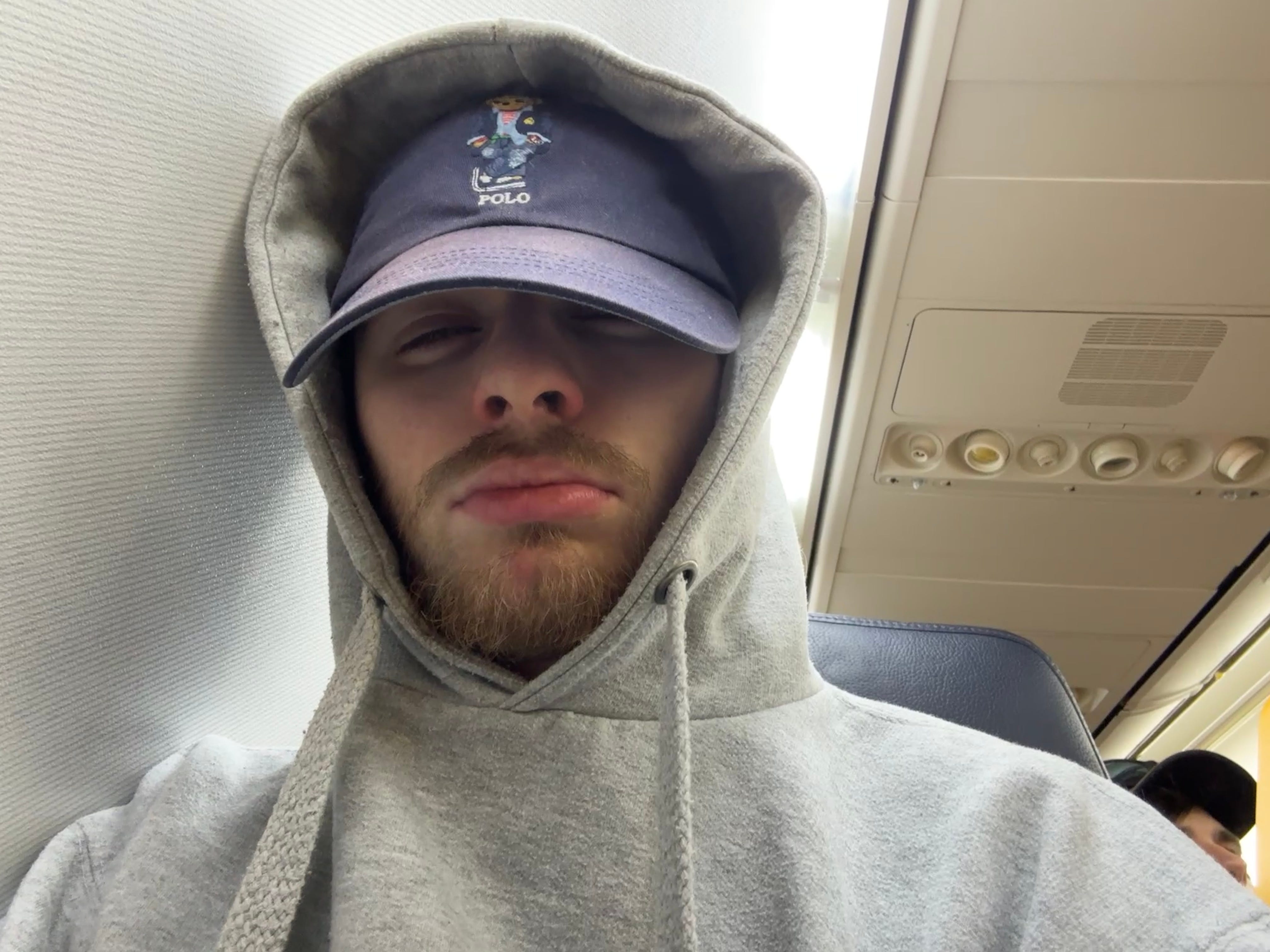 The author, wearing a hoodie and cap, asleep resting against the windowless wall of a Boeing 737