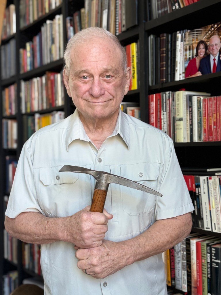 Portrait of H. Keith Melton holding an ice axe in front of a bookshelf.