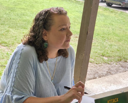The author sits at a table holding a pen in her hand.
