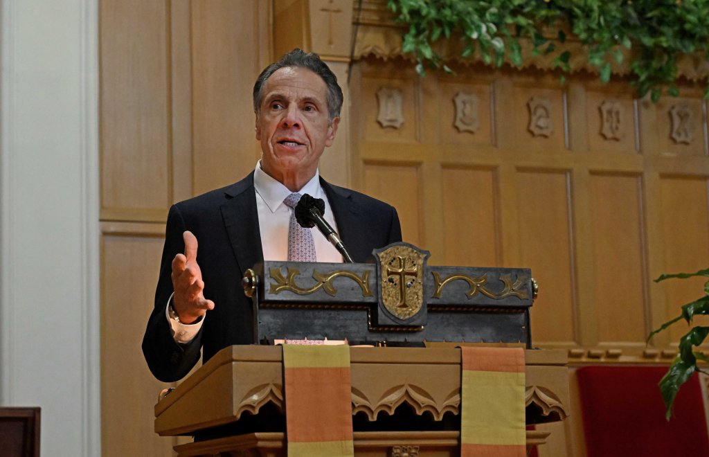 Former Governor Andrew Cuomo speaking at a podium in a church.