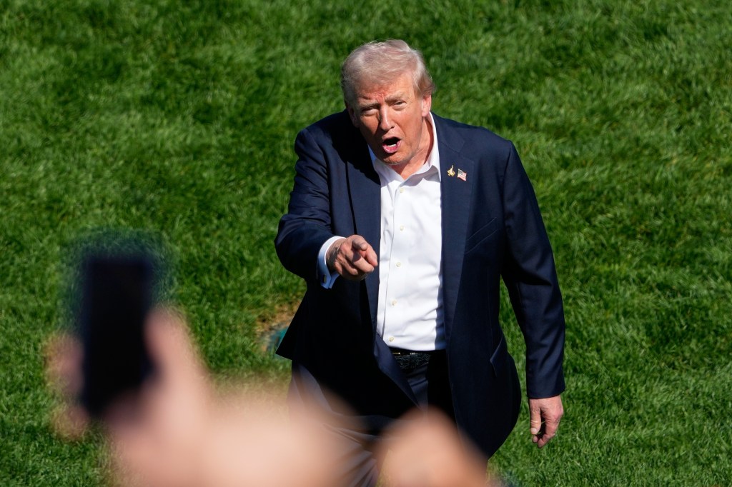 Donald Trump addressing a crowd and pointing at someone in a suit and white shirt with American flag and F-15 jet lapel pins.