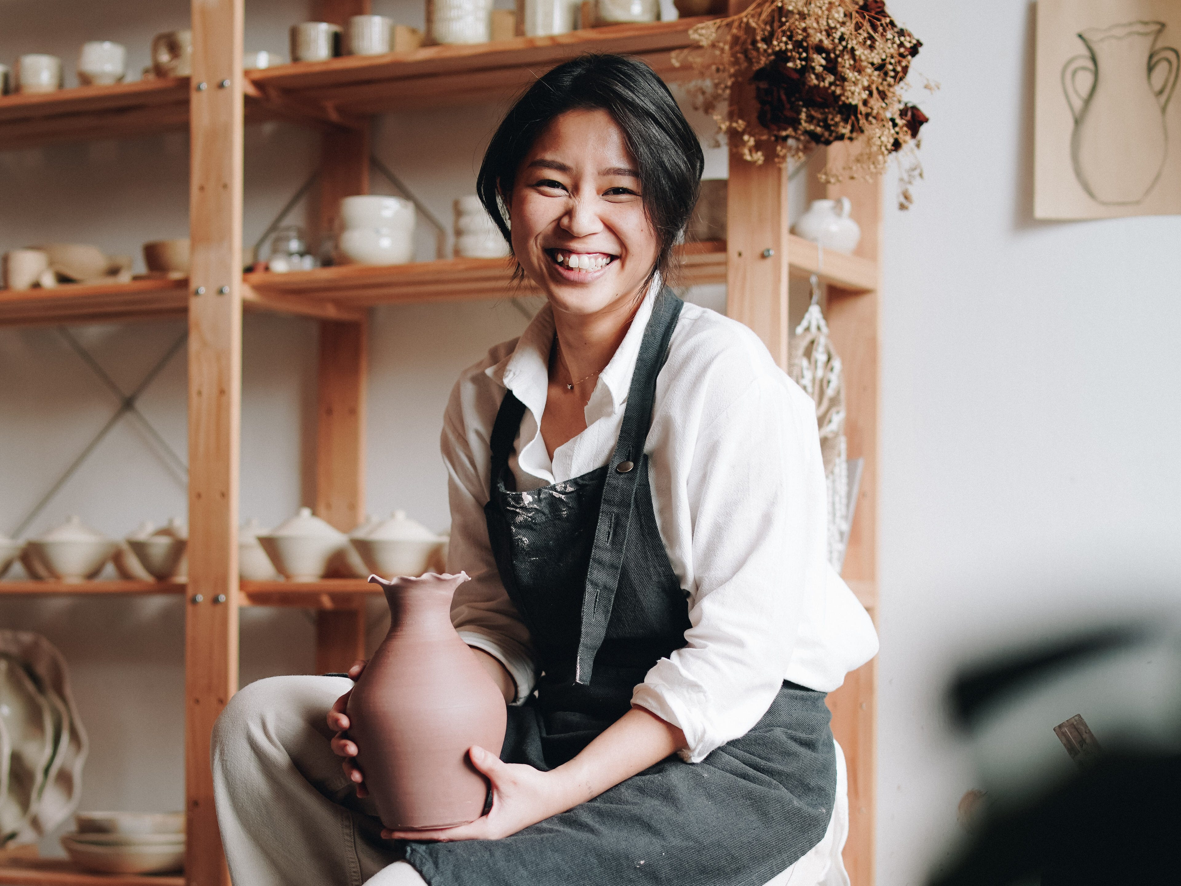 A woman posing with a vase in her studio.