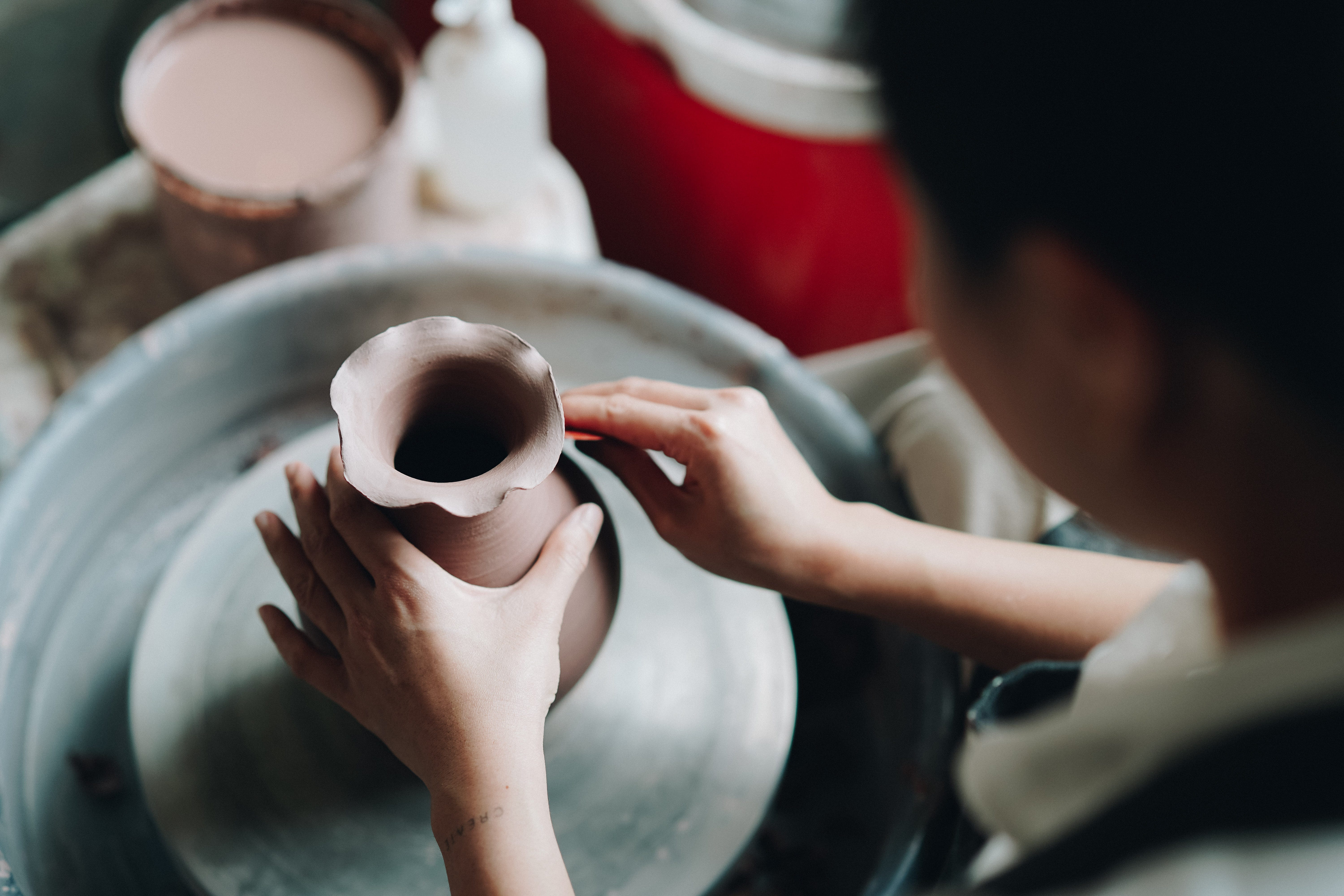 A close up of a woman moulding clay at a pottery wheel.