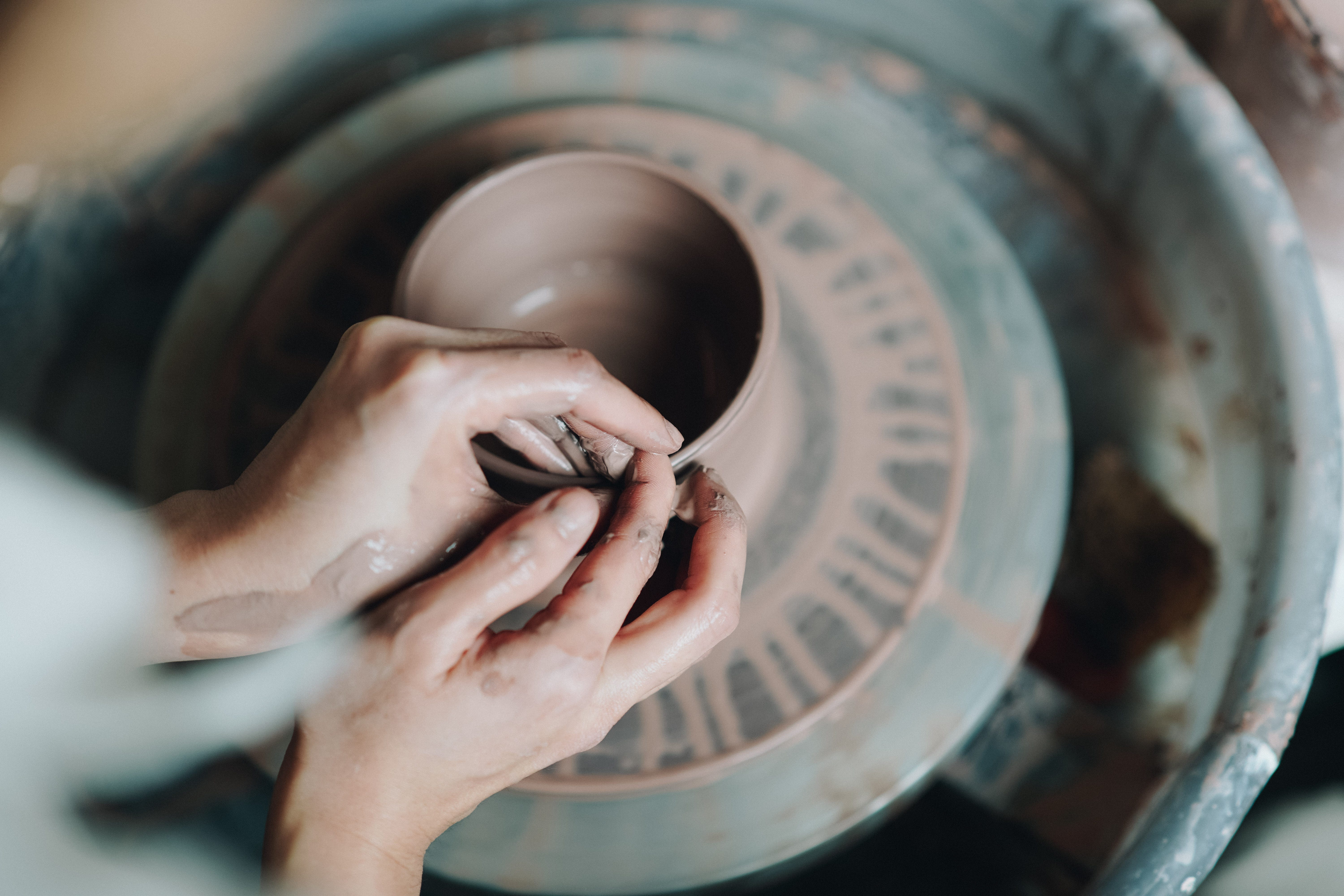 A close up of a woman's hands making pottery on a wheel.