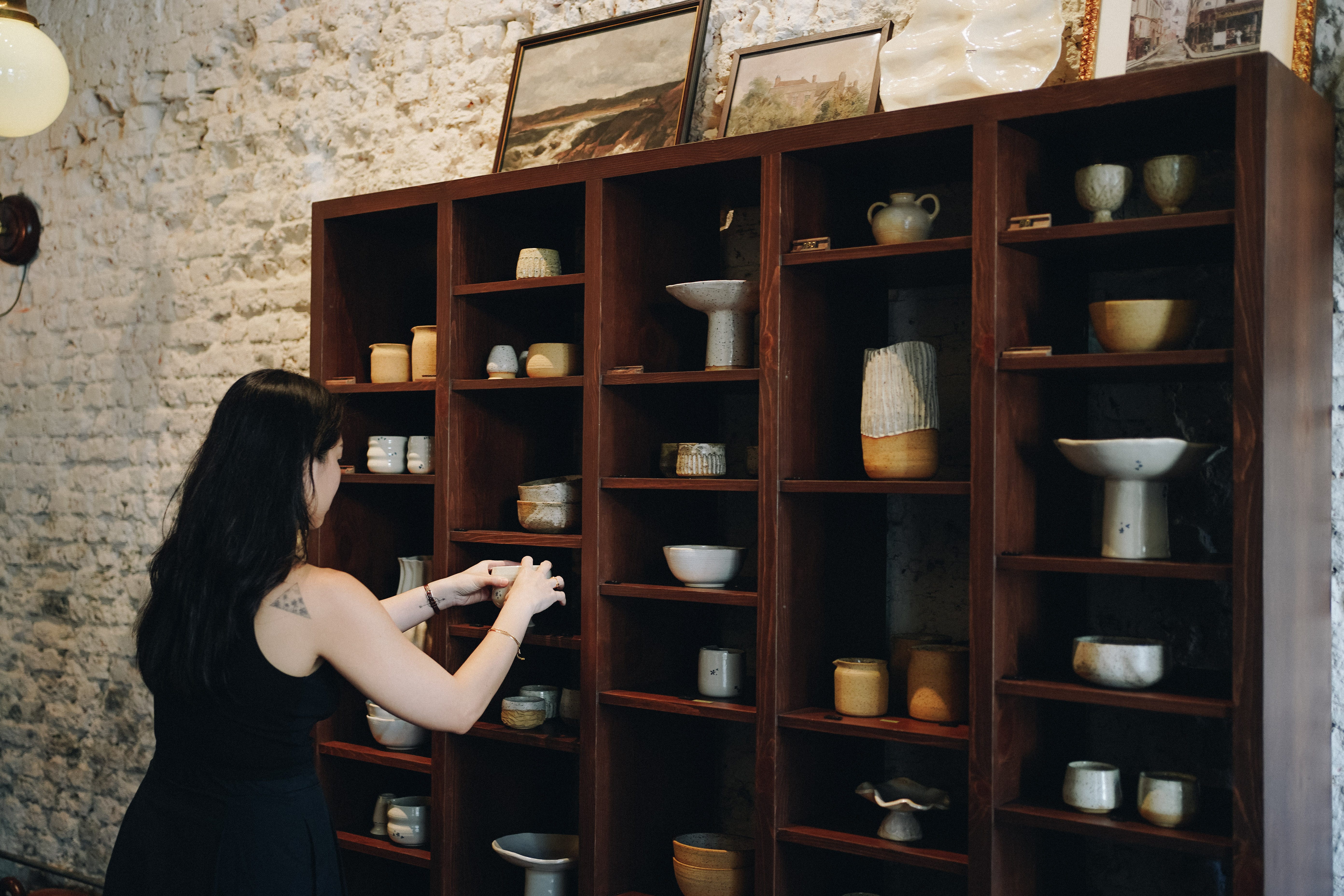 A woman arranging ceramics on a shelf.
