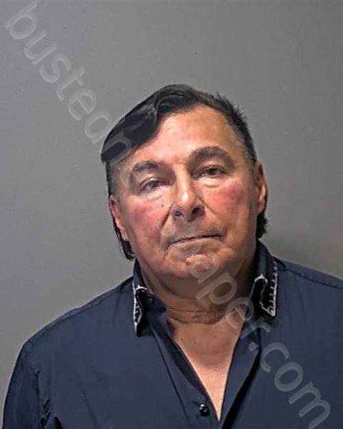 Mugshot of a man with dark hair, a navy blue shirt, and red cheeks.