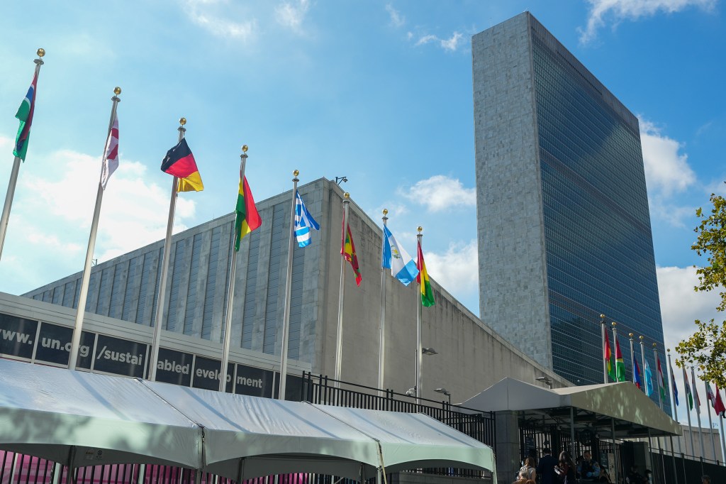 Exterior of the United Nations building with multiple national flags flying.