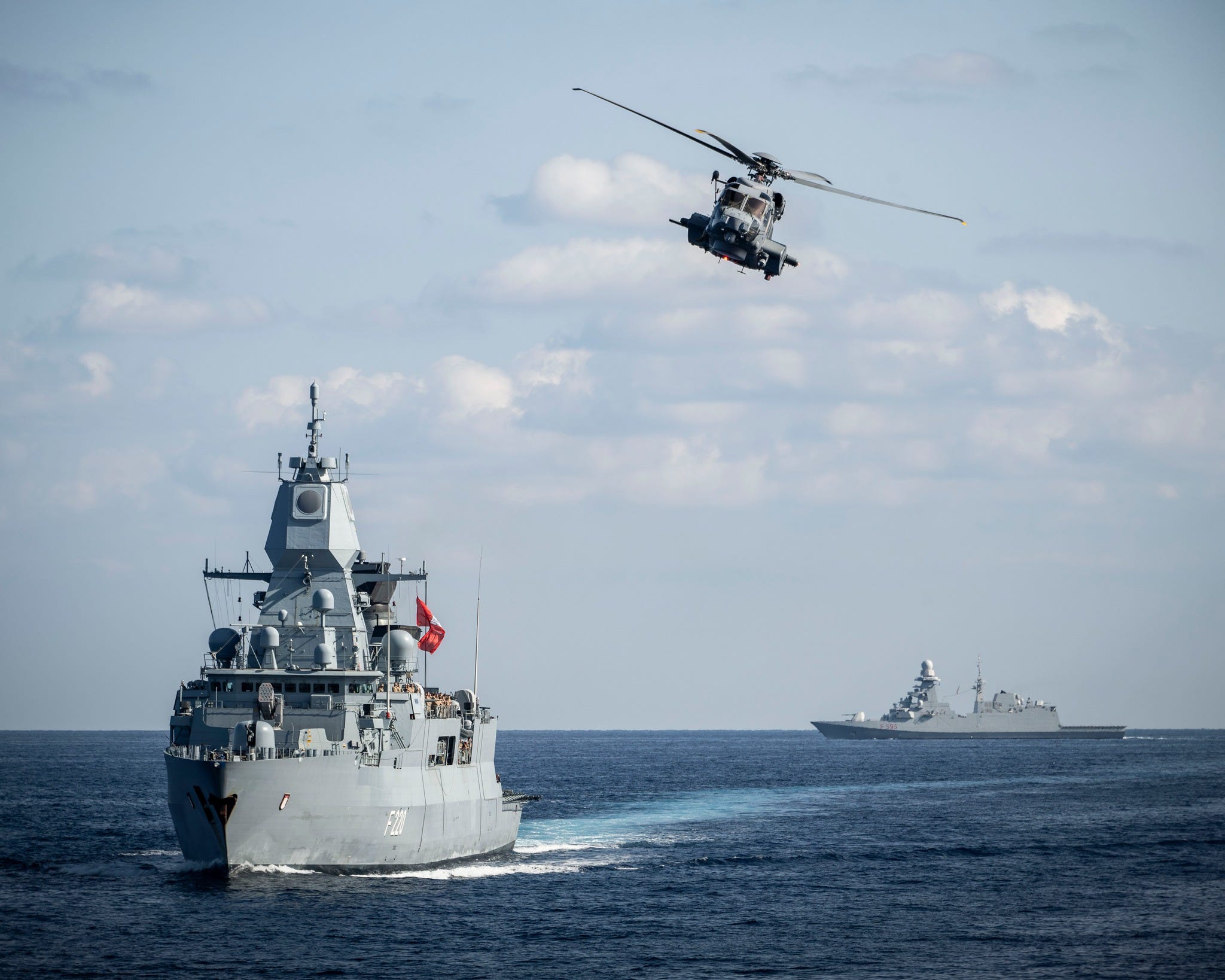A German warship sails under a helicopter.