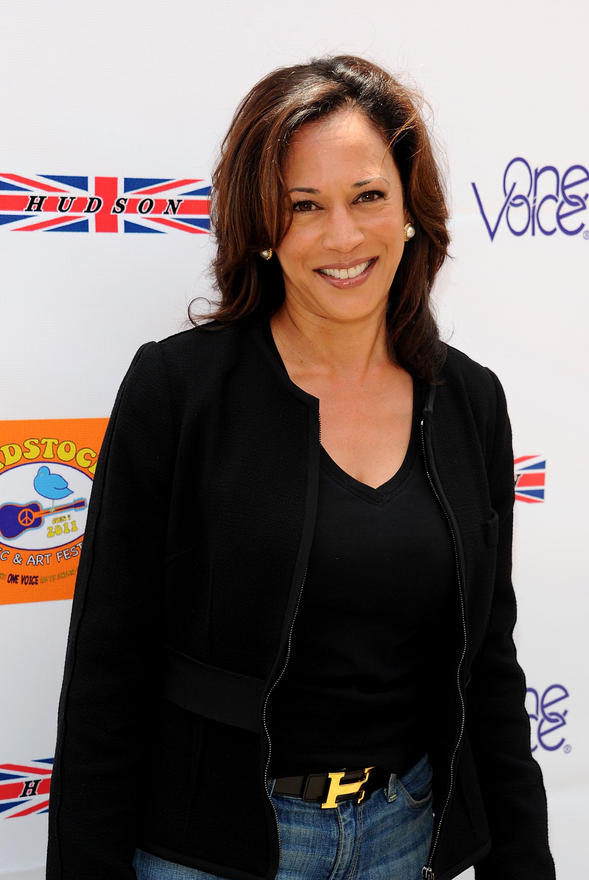 Kamala Harris in a black shirt, black jacket, and jeans, with an Hermes belt.