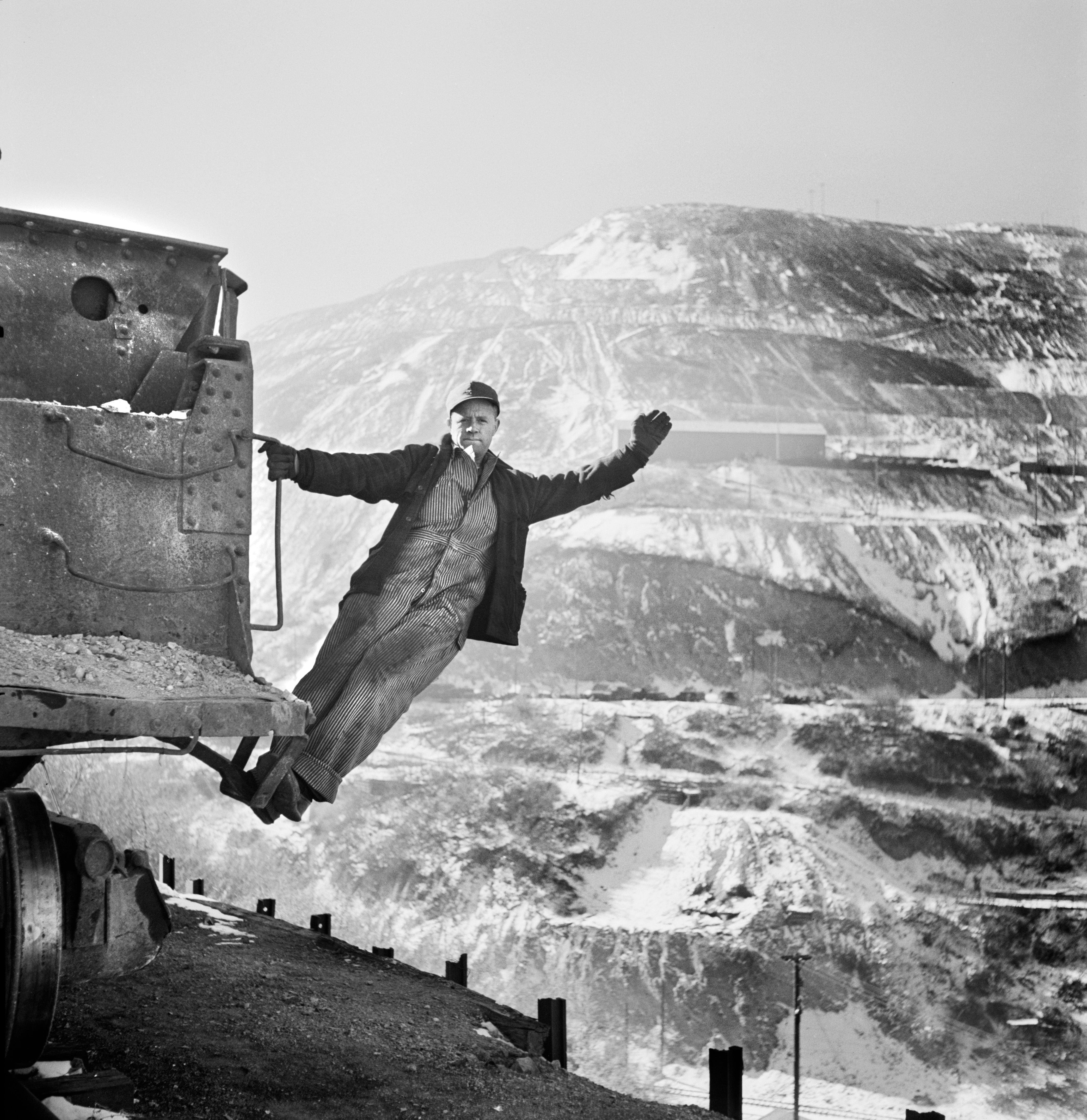 A train brakeman signals from a train and hangs off of it