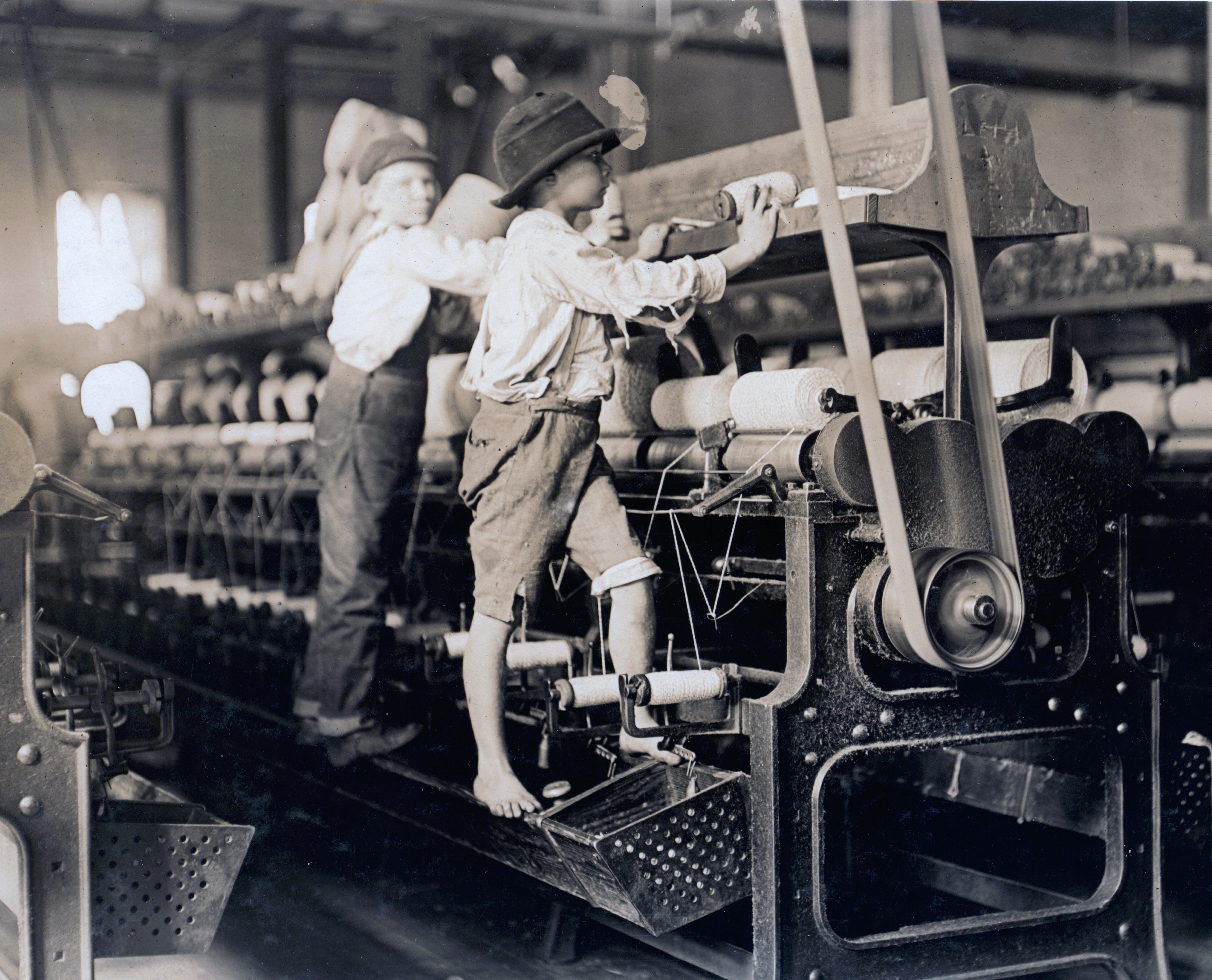 Young boys, one barefoot and wearing a hat, stand on top of a large machine