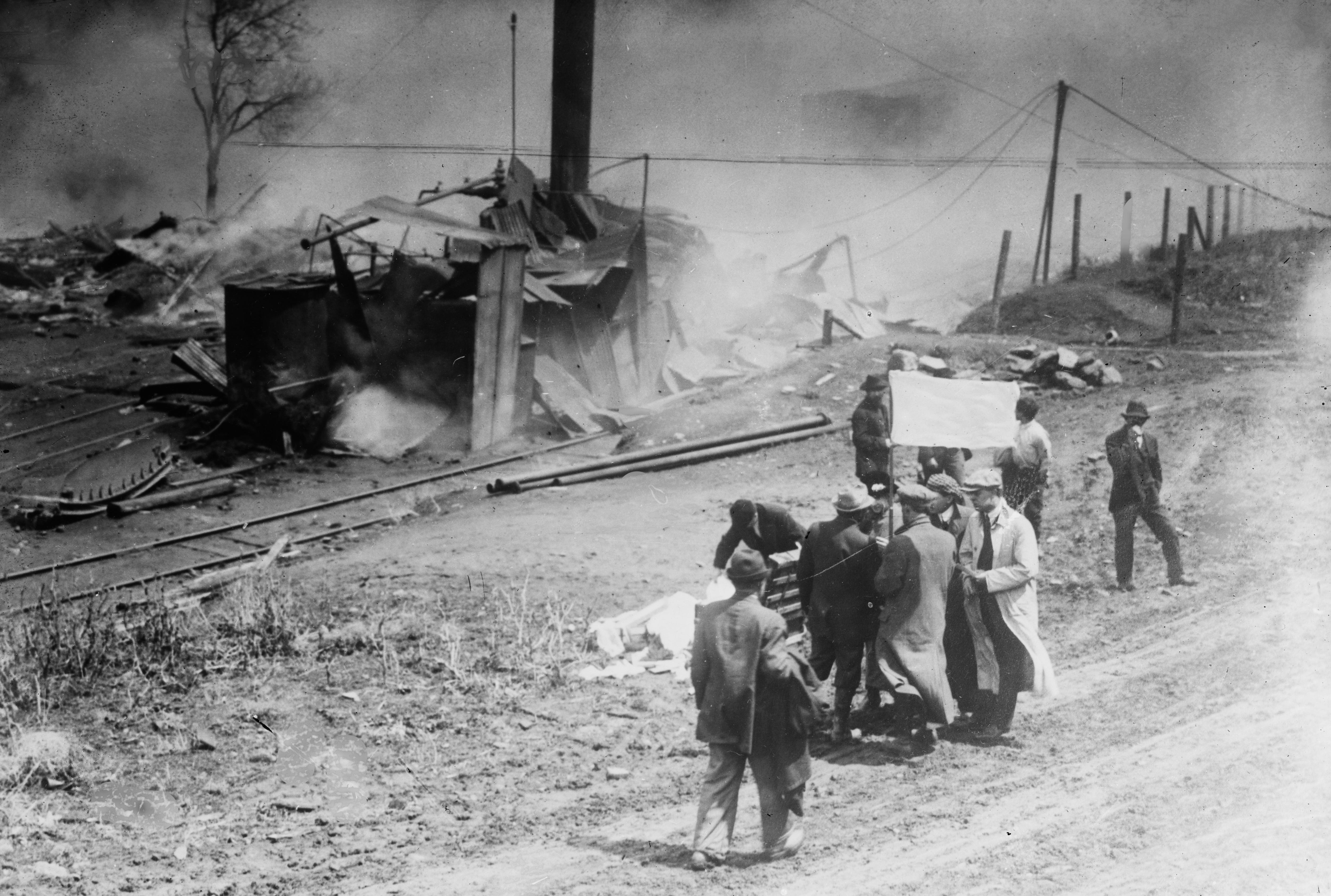 Several people carry items near a collapsed building