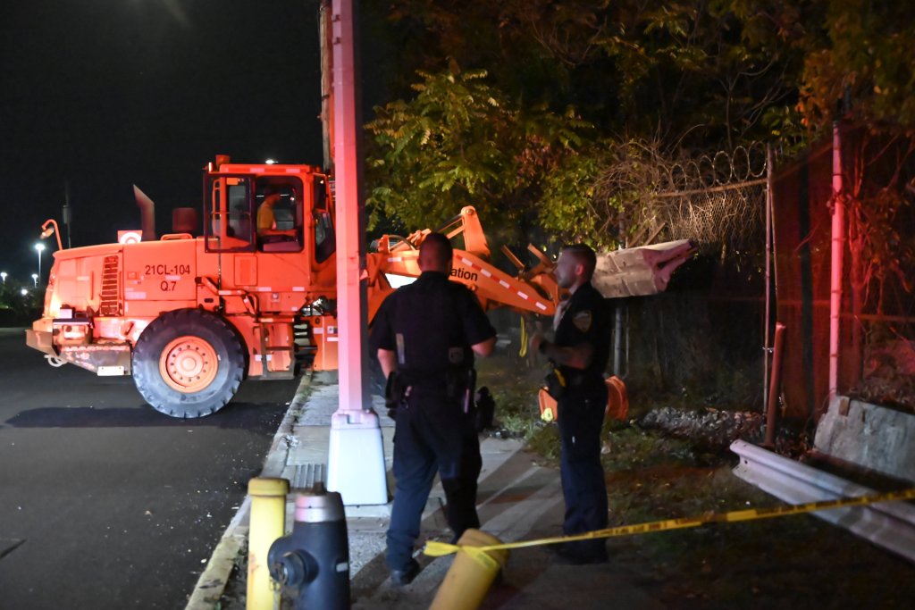 Two police officers stand near an orange construction vehicle at night.