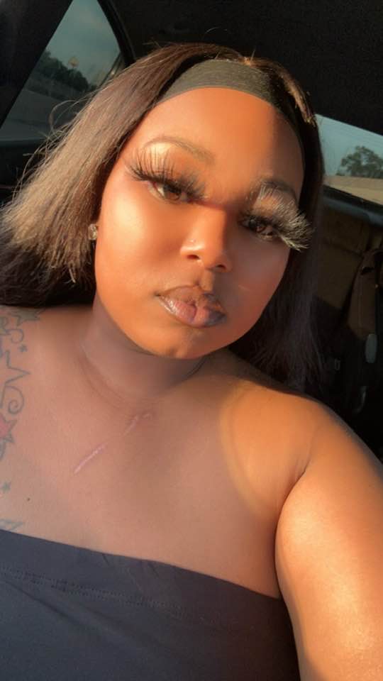 A woman with long eyelashes, a black headband, and a tattoo on her right shoulder in a car.
