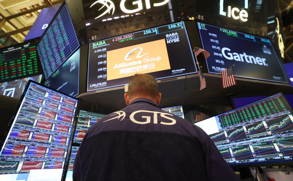 A trader in a GTS shirt facing away from the camera, surrounded by screens displaying stock market data, including Alibaba Group and Gartner.