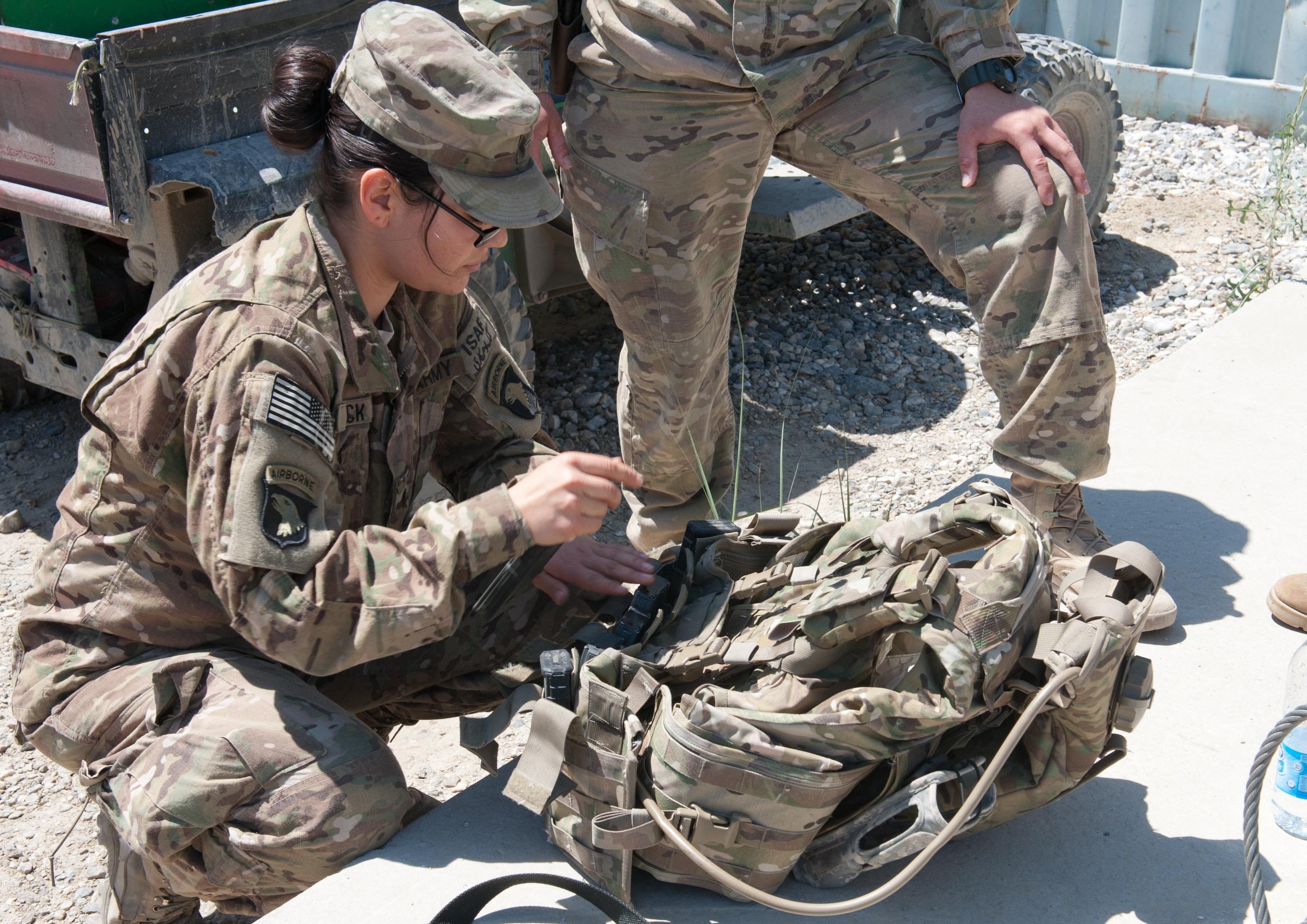 A soldier secures equipment to her body armor.
