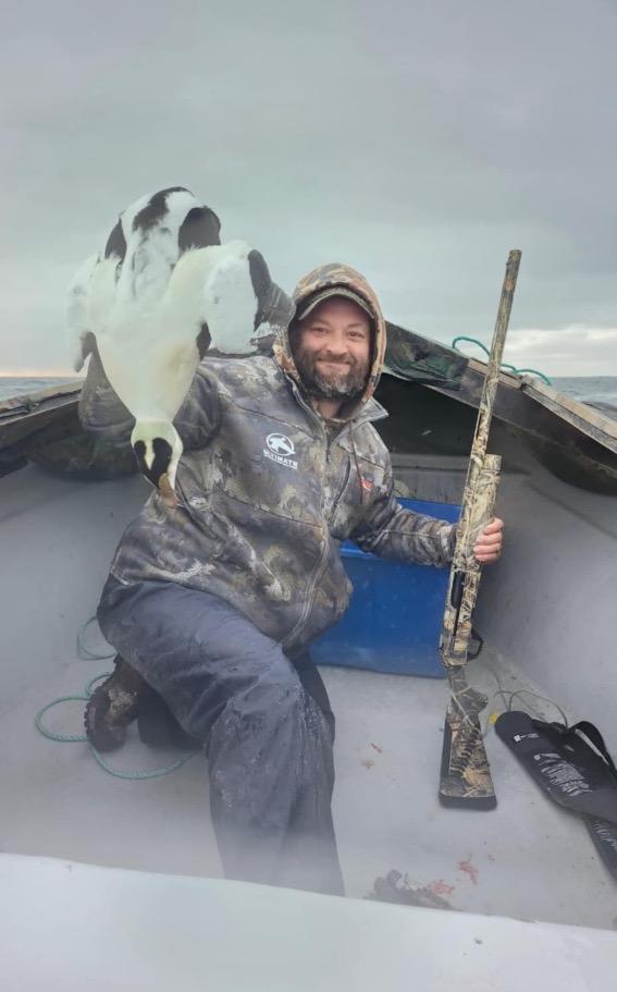 Thomas Jacob Sanford holding a dead gannet and a shotgun in a boat.