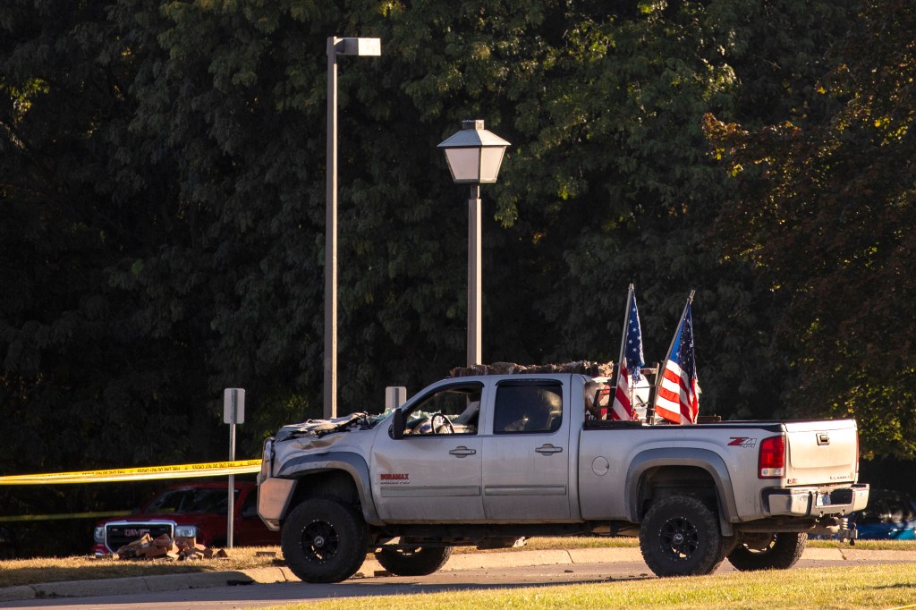The suspect's damaged silver pickup truck with two American flags in the bed, parked near a yellow 