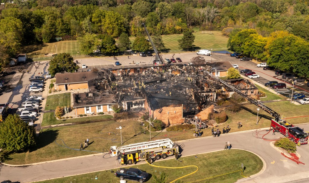 Aerial view of a burnt church building surrounded by emergency vehicles and personnel.
