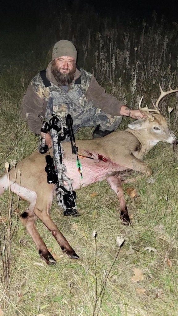 Thomas Jacob Sanford, aka Jake Sanford, kneeling next to a dead deer with an arrow in its side.
