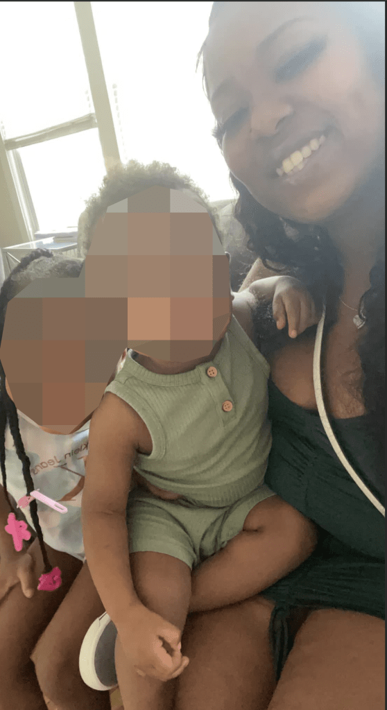 A young woman smiles and sits with two young children.
