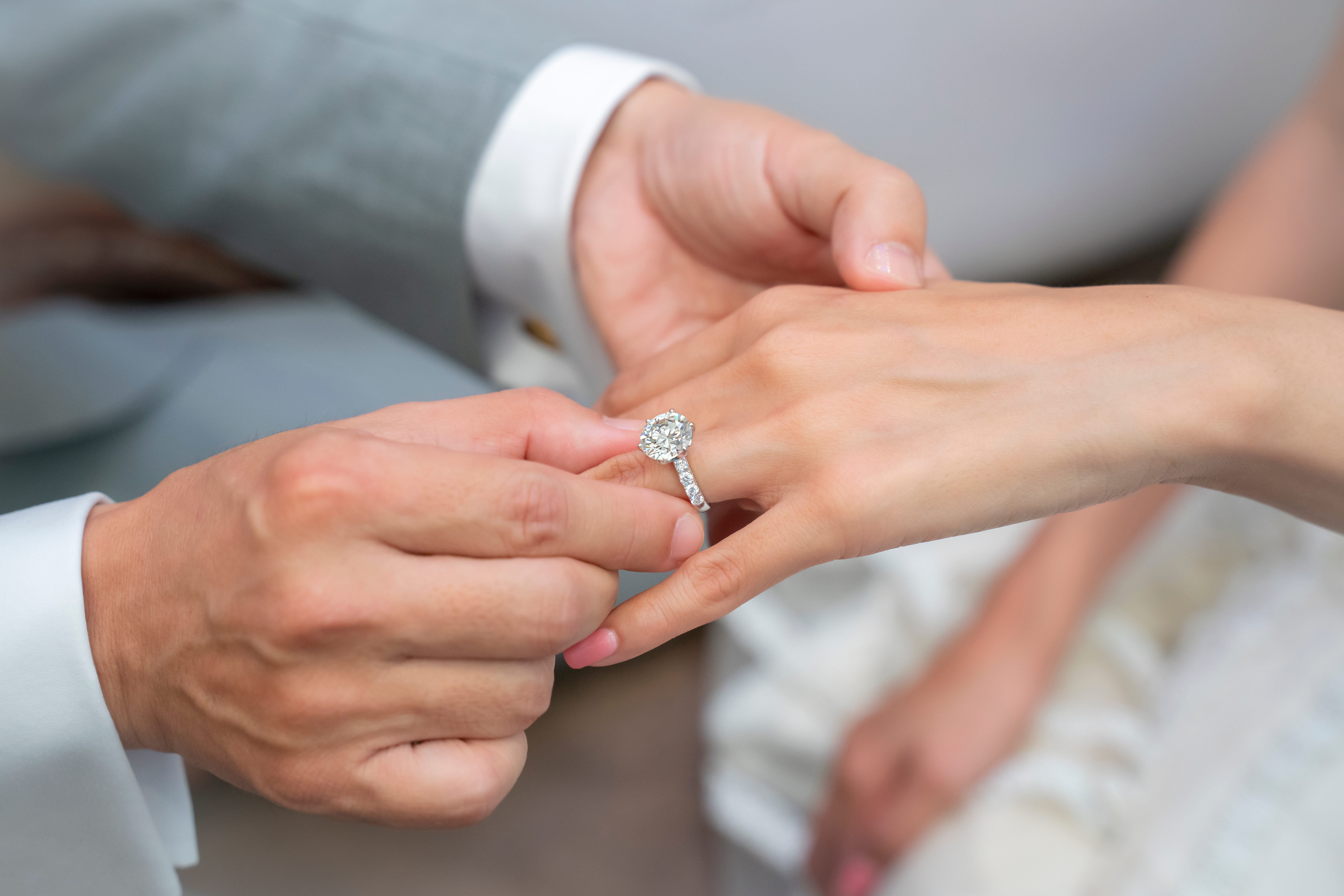 A man slides a diamond engagement ring with an eternity band onto a woman's finger.