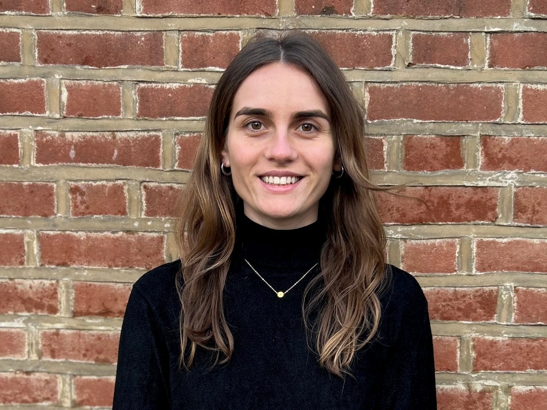 A young woman stands in front of a brick wall.