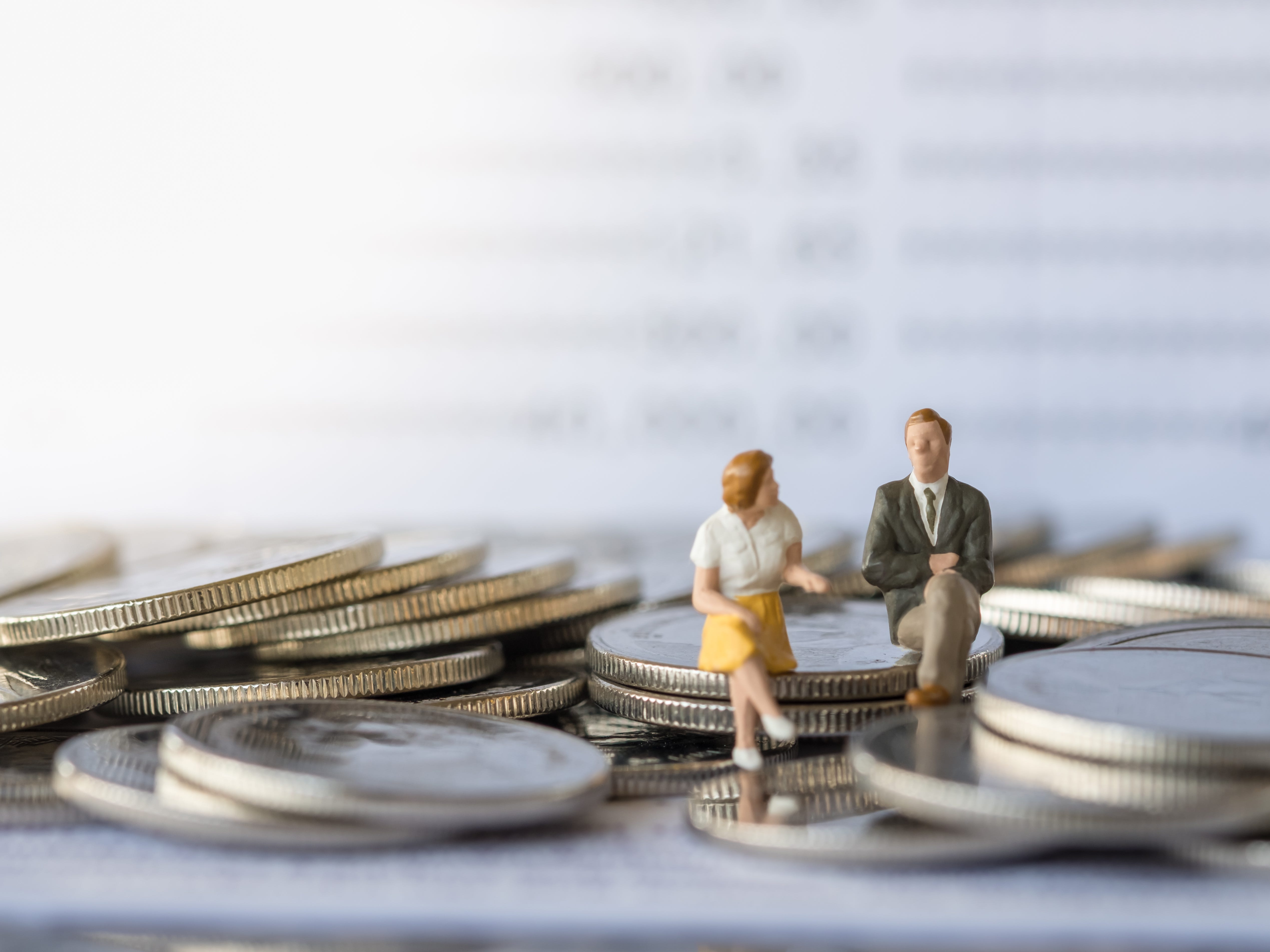 Miniature figurines of a man and woman sitting on a pile of coins.