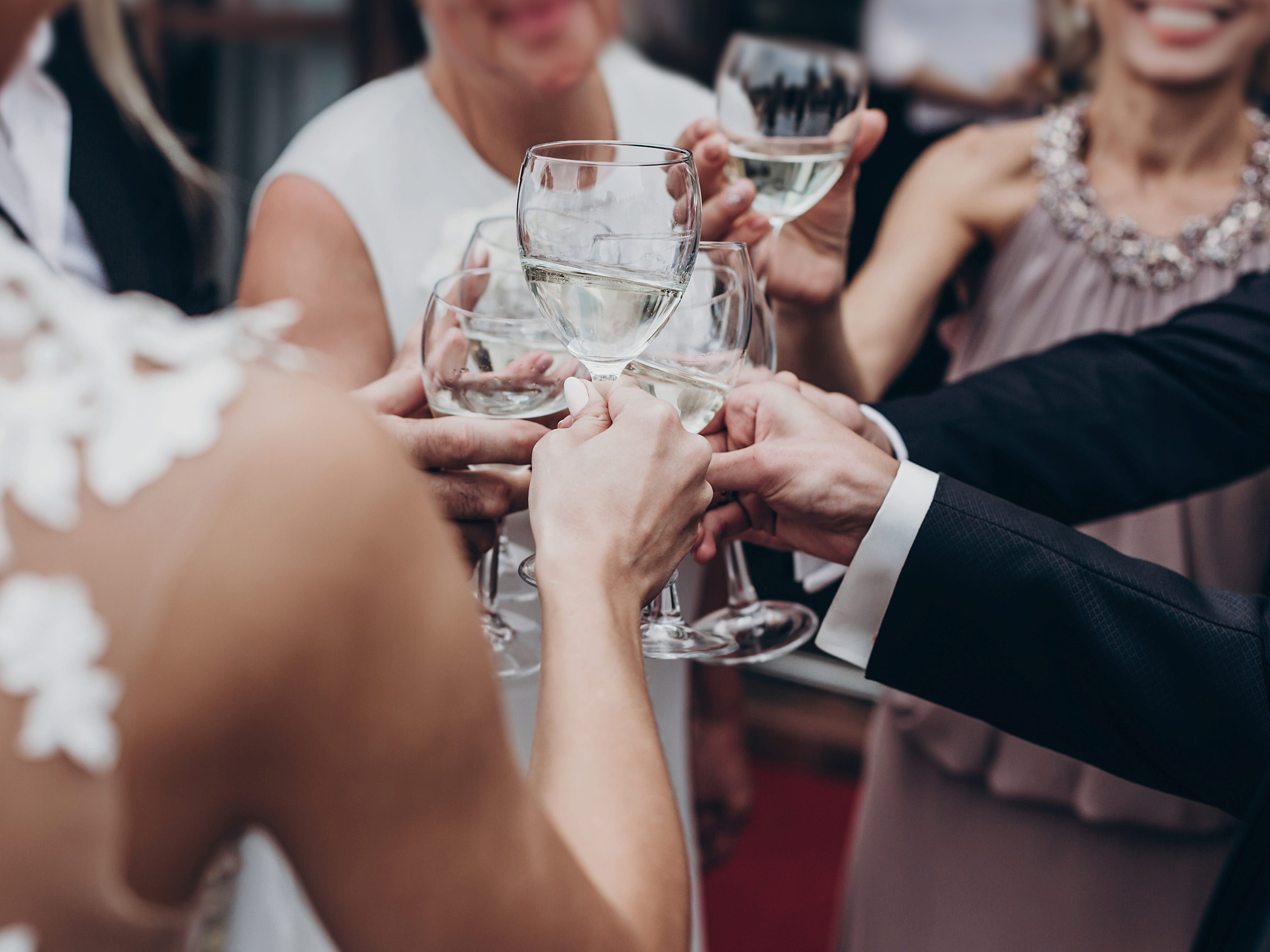 A close-up image of a bride toasting glasses with guests at her wedding. The bride's back is to the camera.