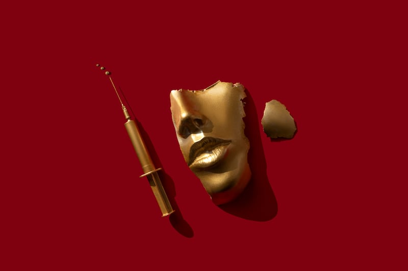 Half a gold face next to a gold syringe; metaphor for plastic surgery and injectables