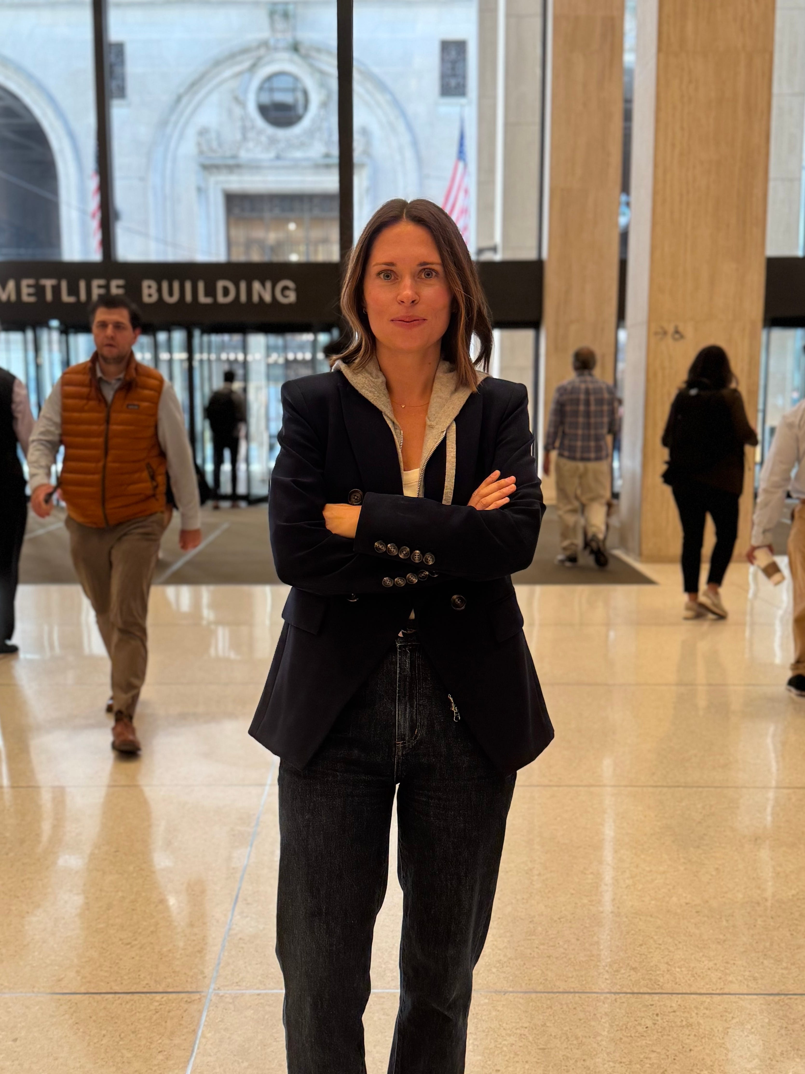 A woman wearing black clothing stands with arms crossed in an office lobby