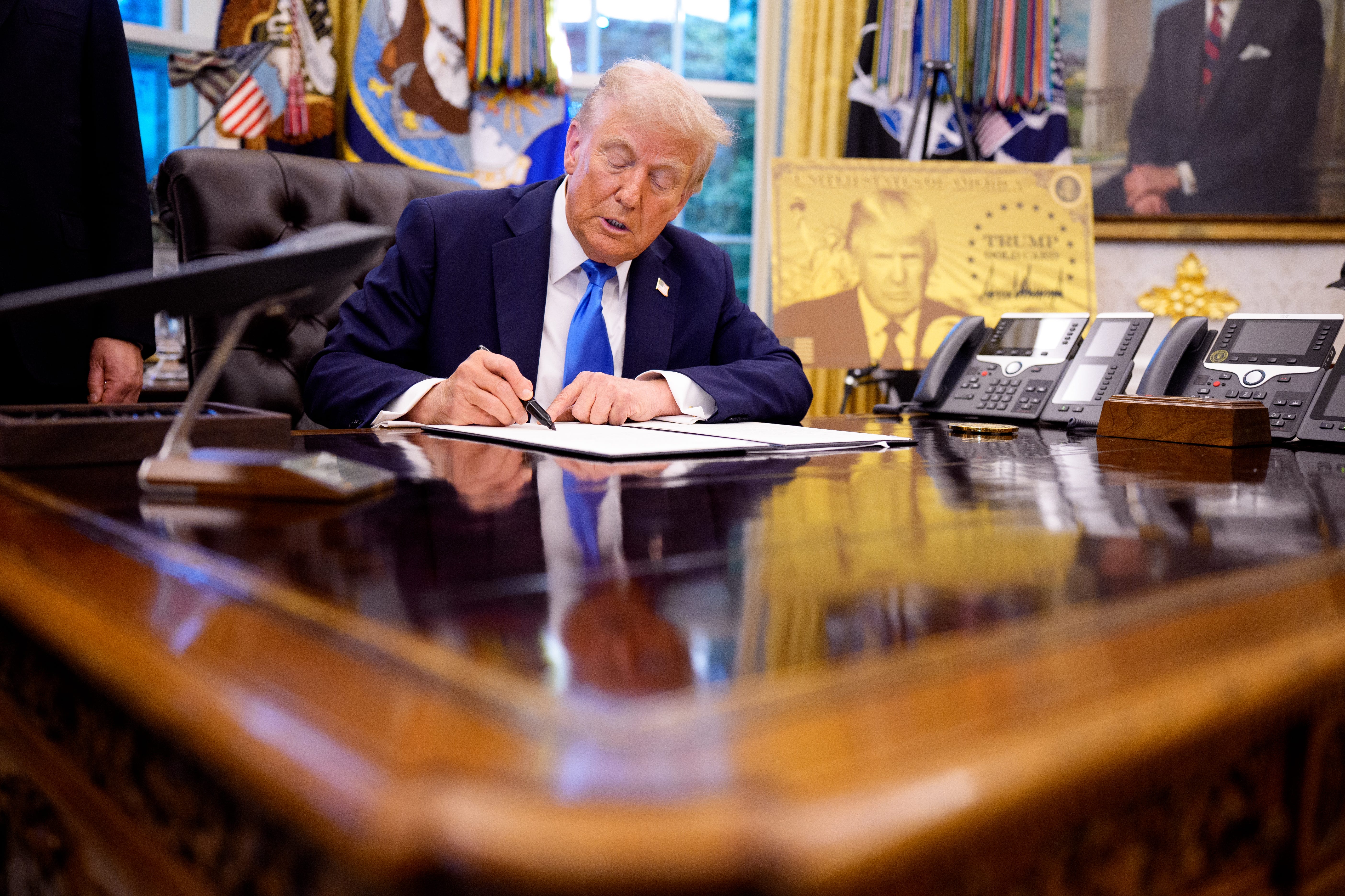 Trump at the desk in a blue tie, signing an executive order.
