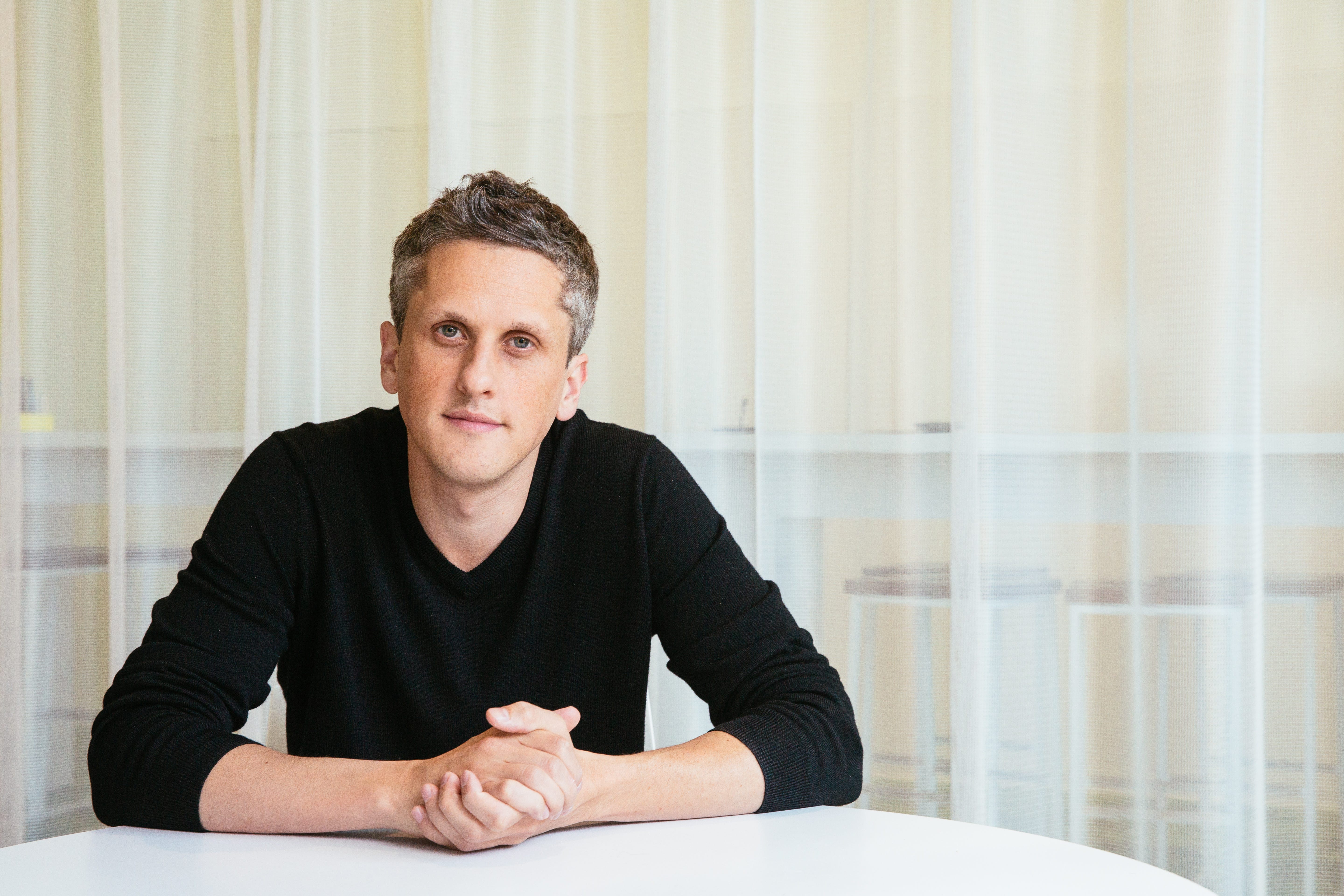 Aaron Levie is wearing a long-sleeved black shirt and has his hands clasped together.