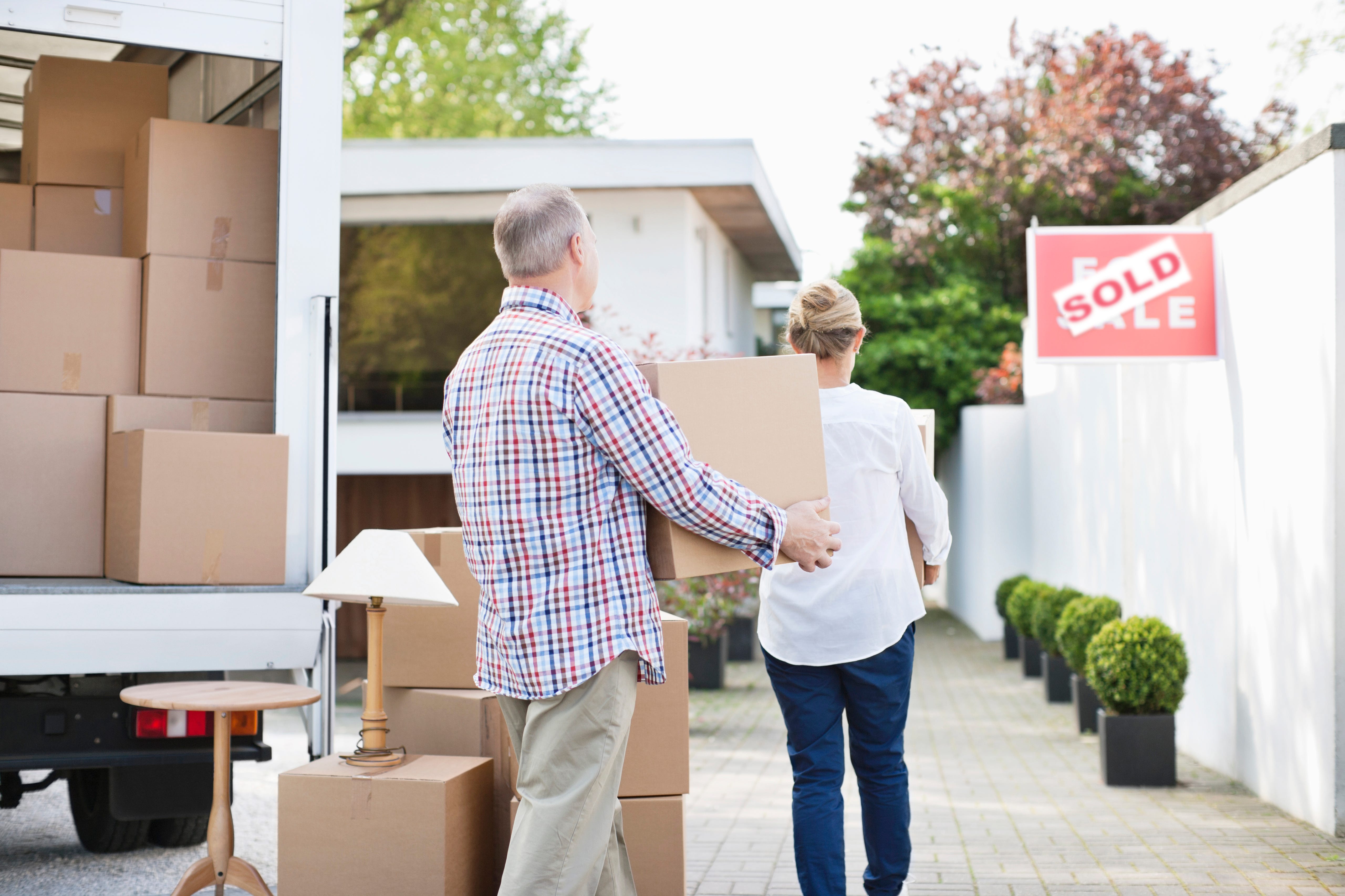 A couple with moving boxes, walking up a driveway.