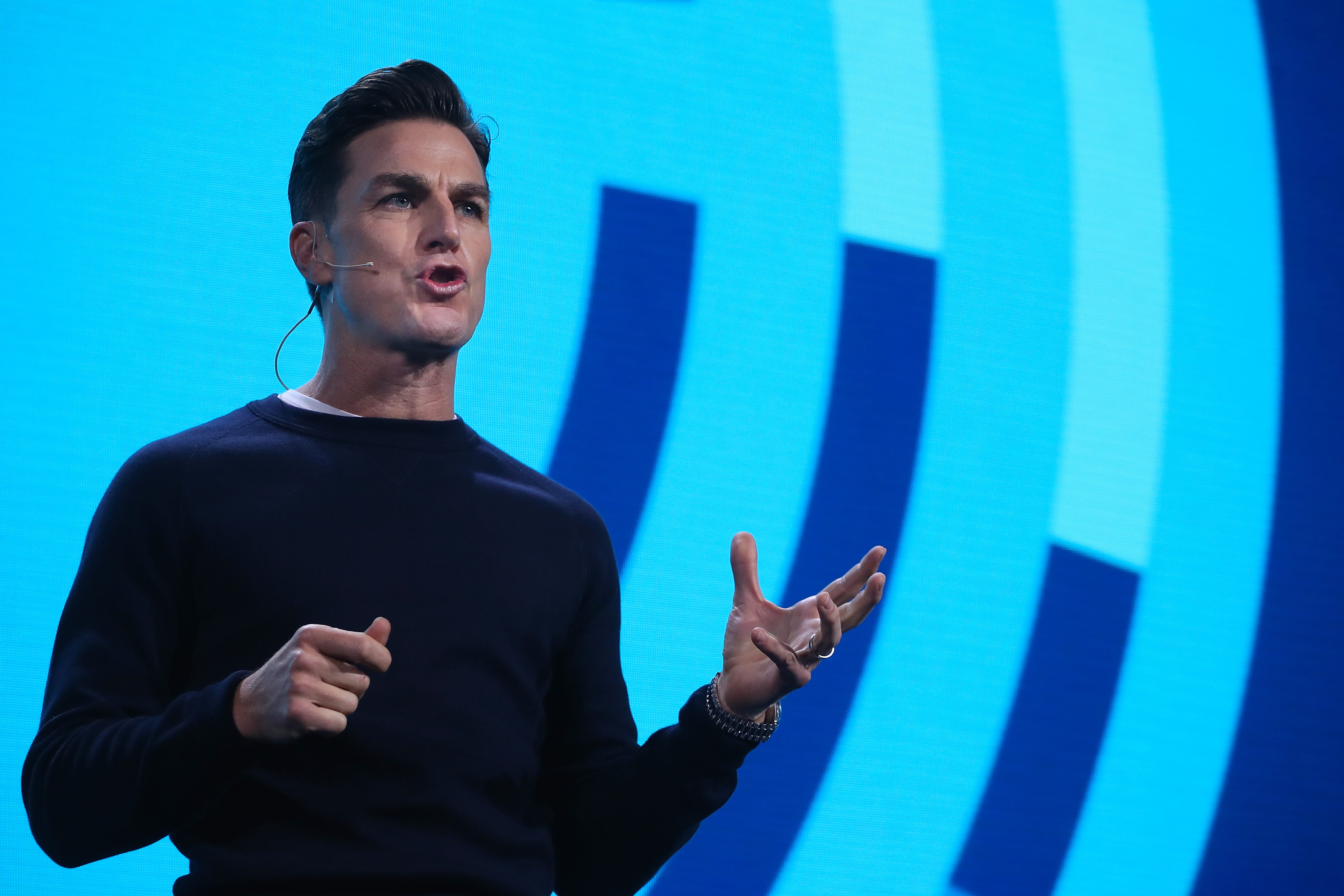 a man in a black shirt presents onstage in front of blue background