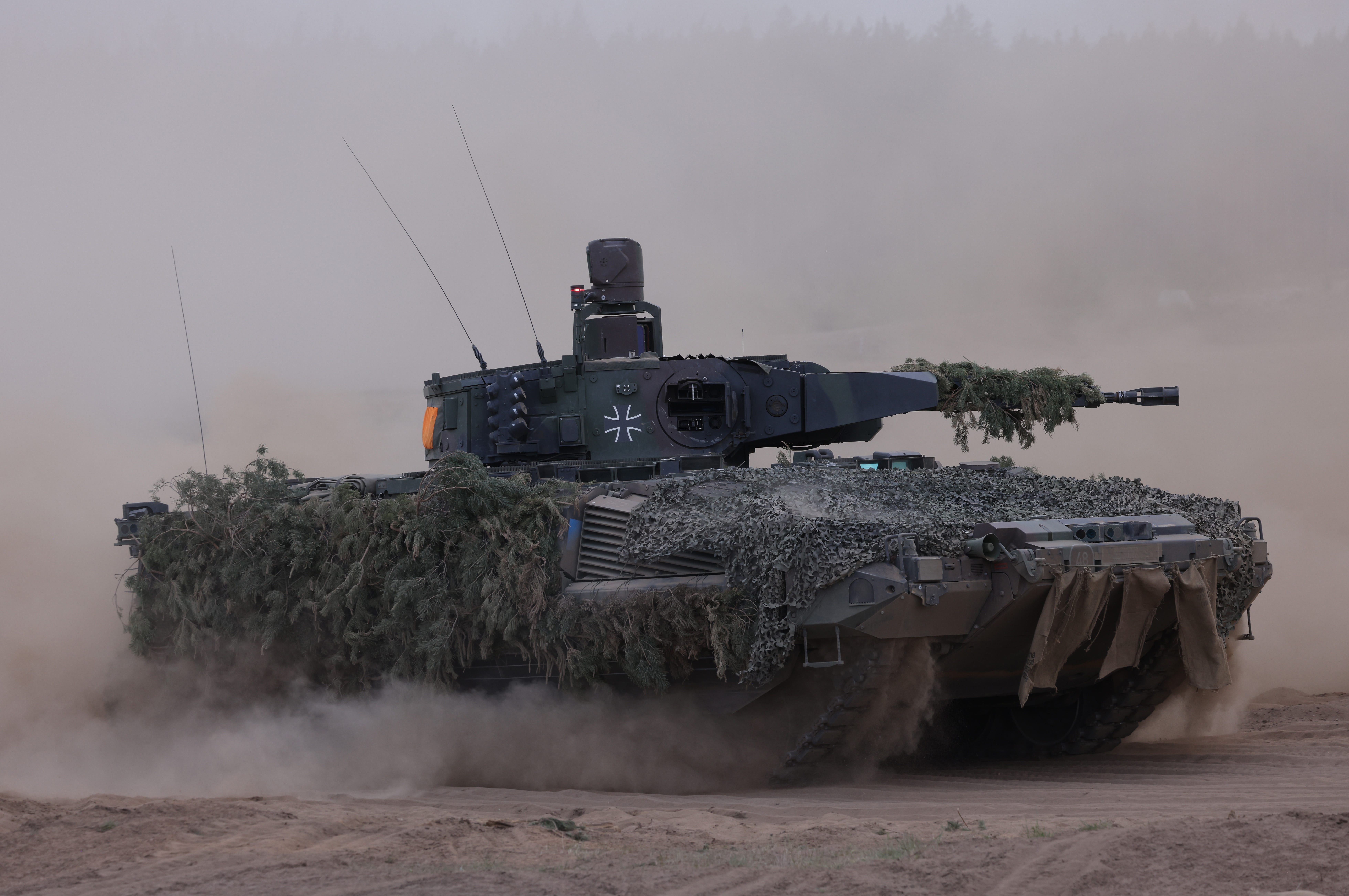 An armored vehicle driving on a dusty road with camoflage netting on top