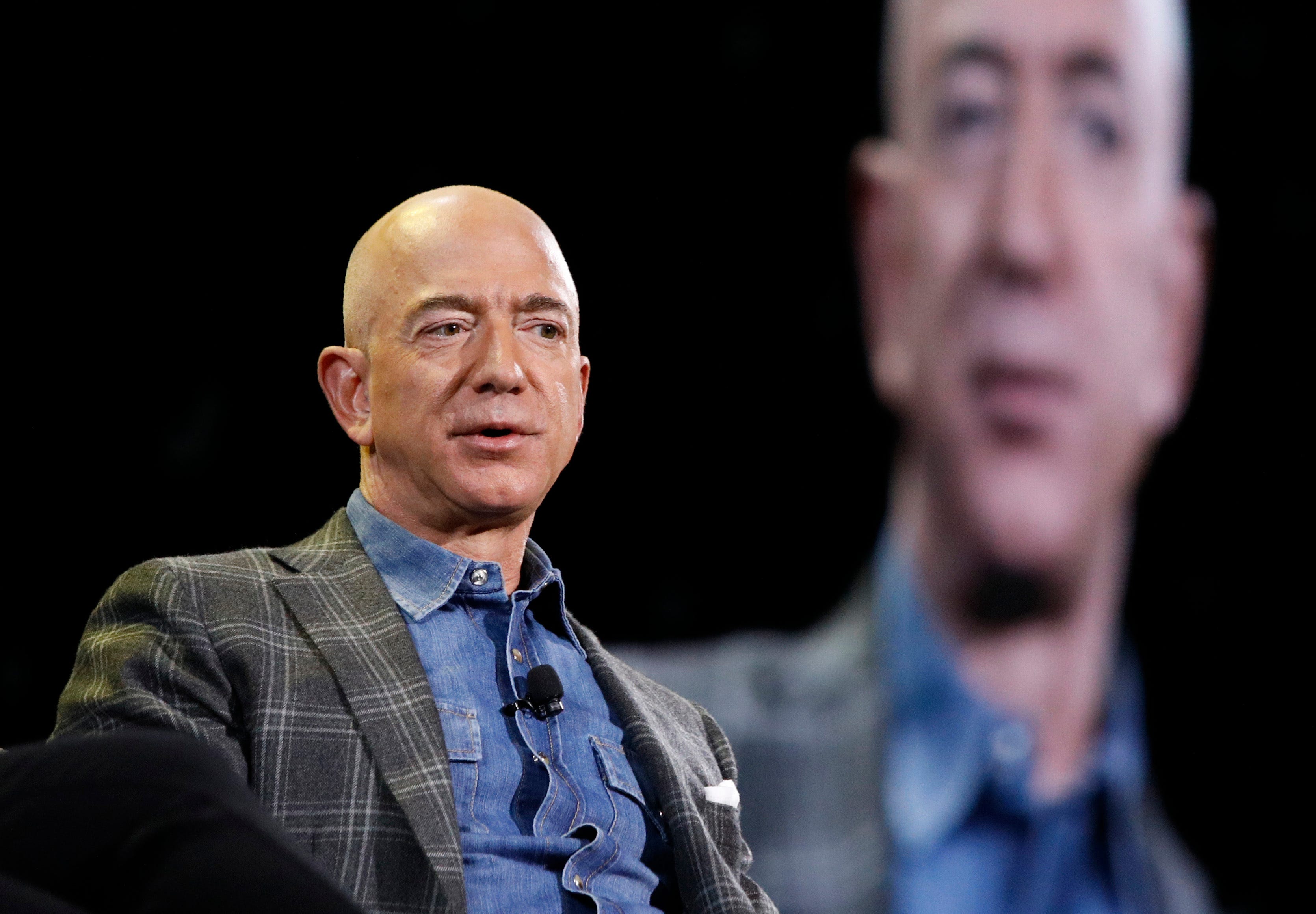 Jeff Bezos speaking in front of a blurred out image of himself.