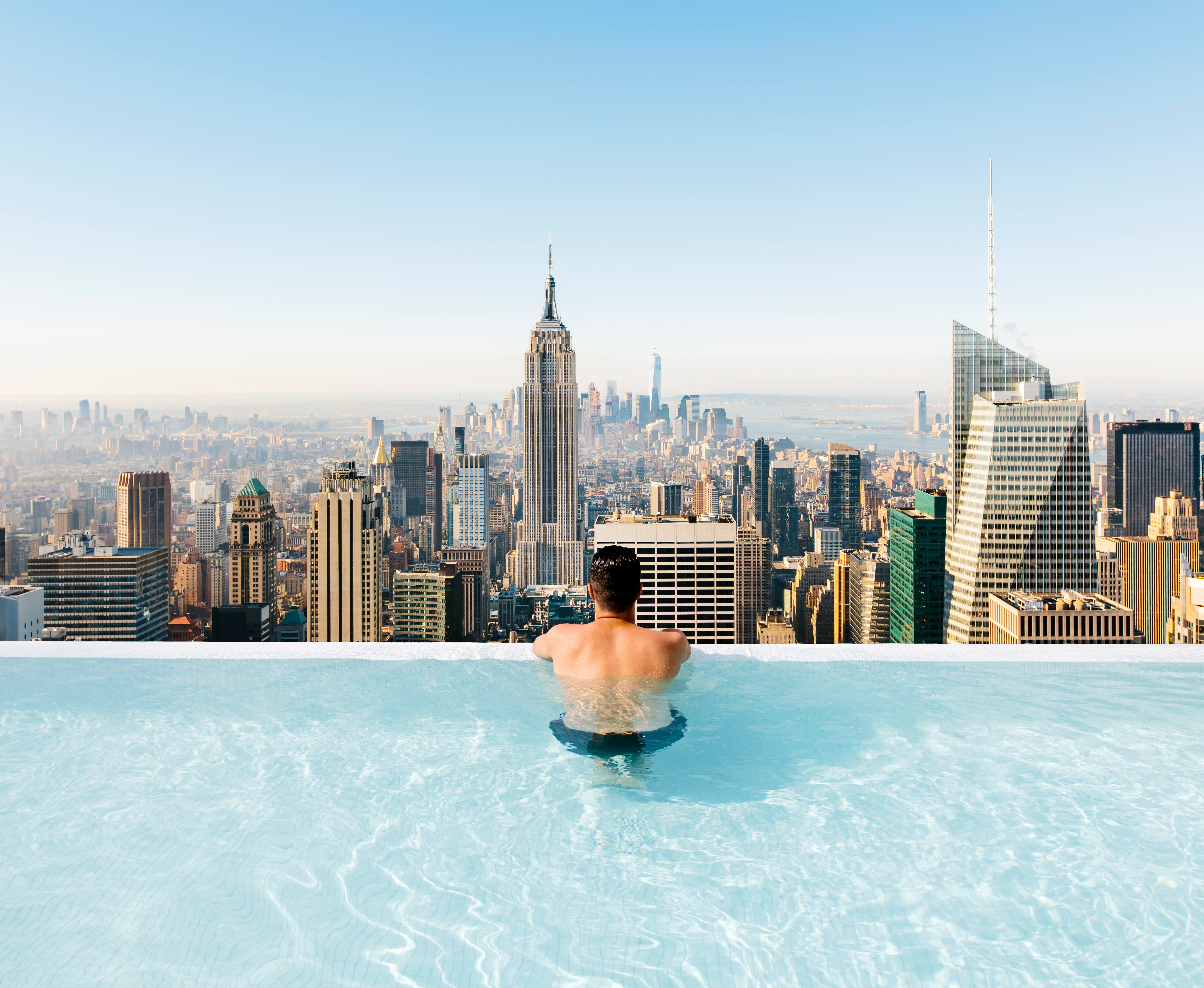 Young man relaxing in a swimming pool with view towards New York City skyline.