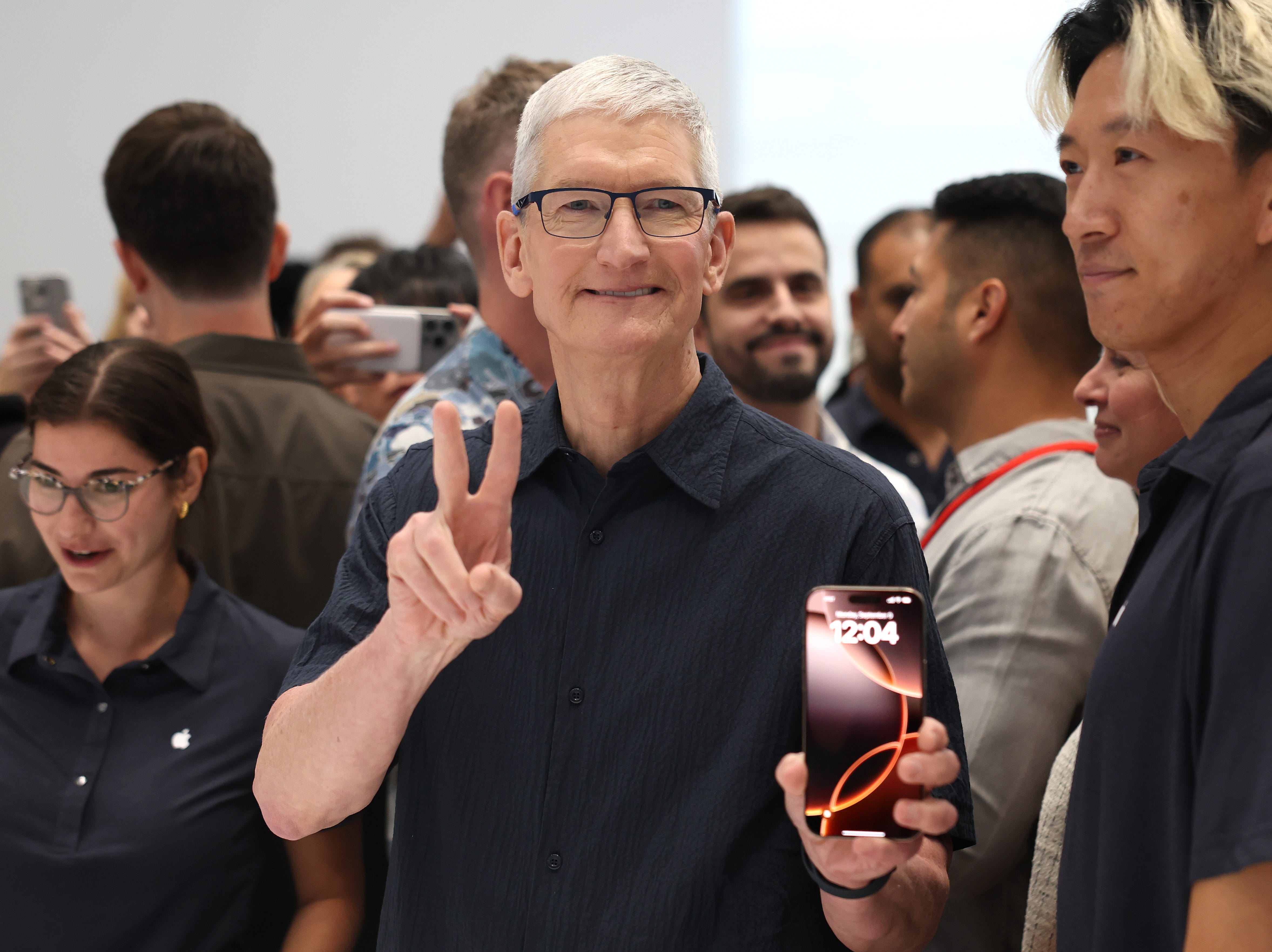 Tim Cook holding up an iPhone 16 at Apple headquarters.