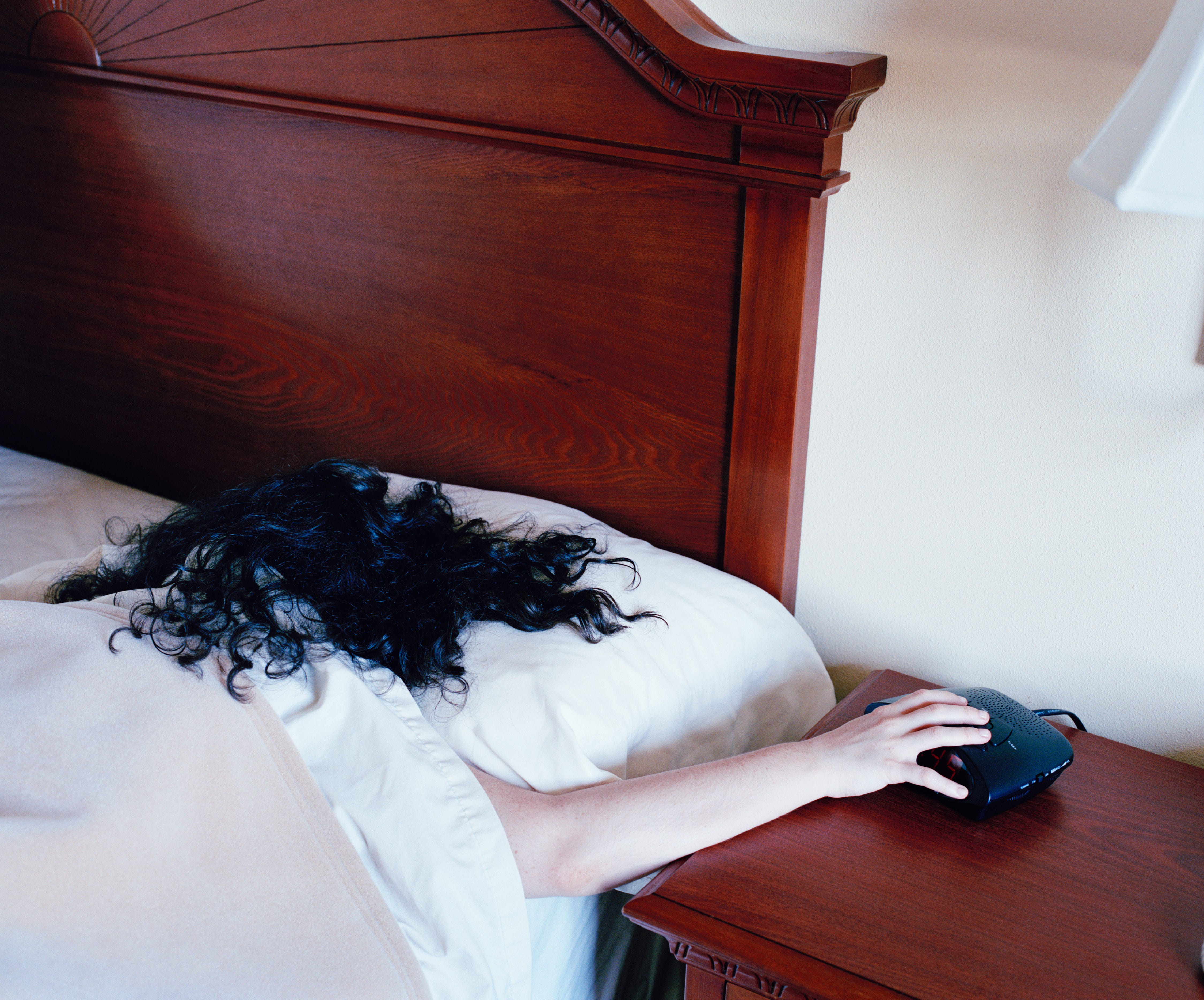 A woman reached from her bed to turn off a clock alarm.
