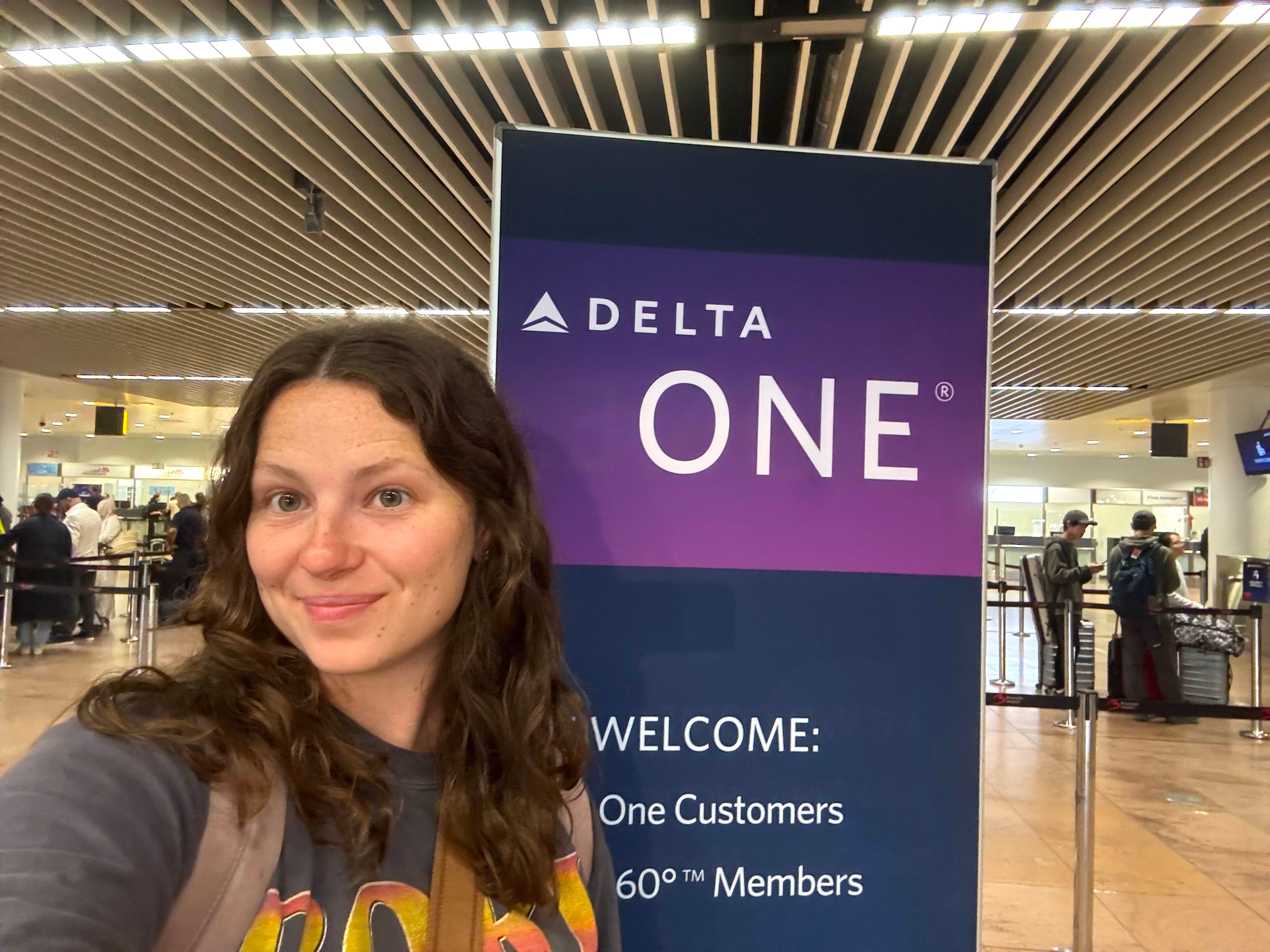 A selfie of a woman standing in front of a Delta One sign.
