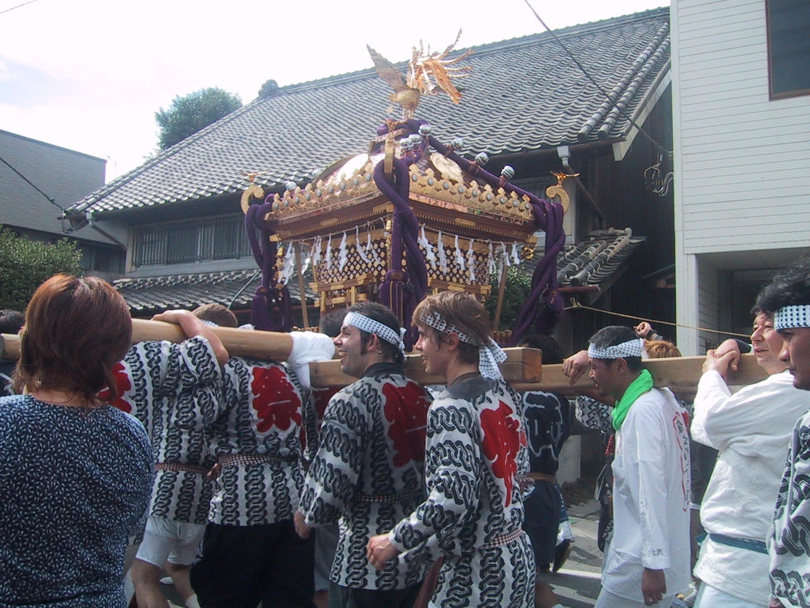 group of people marching down streets in Japan carrying a gold portable shrine