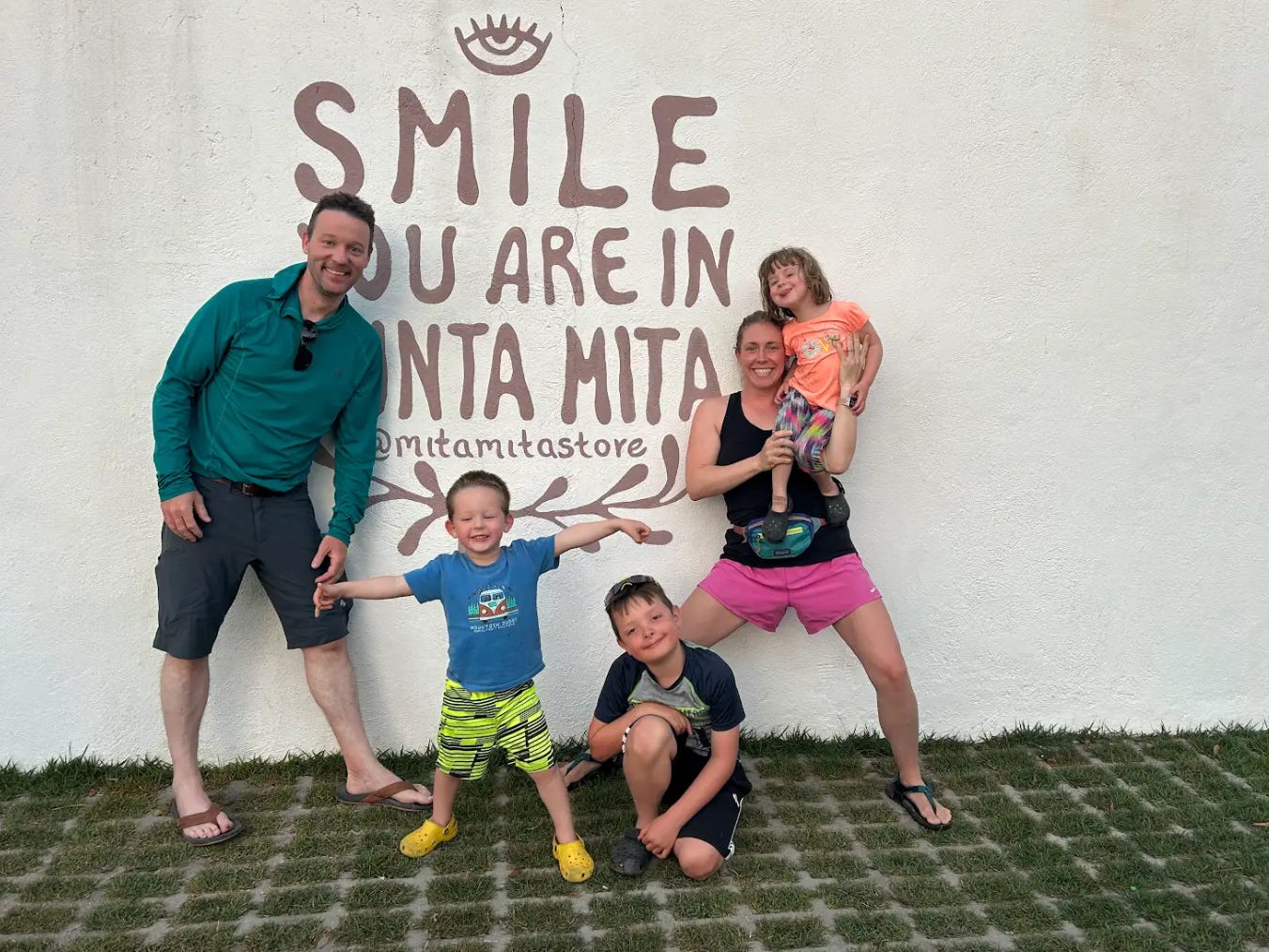 Family of five posing playfully in front of a wall that says 