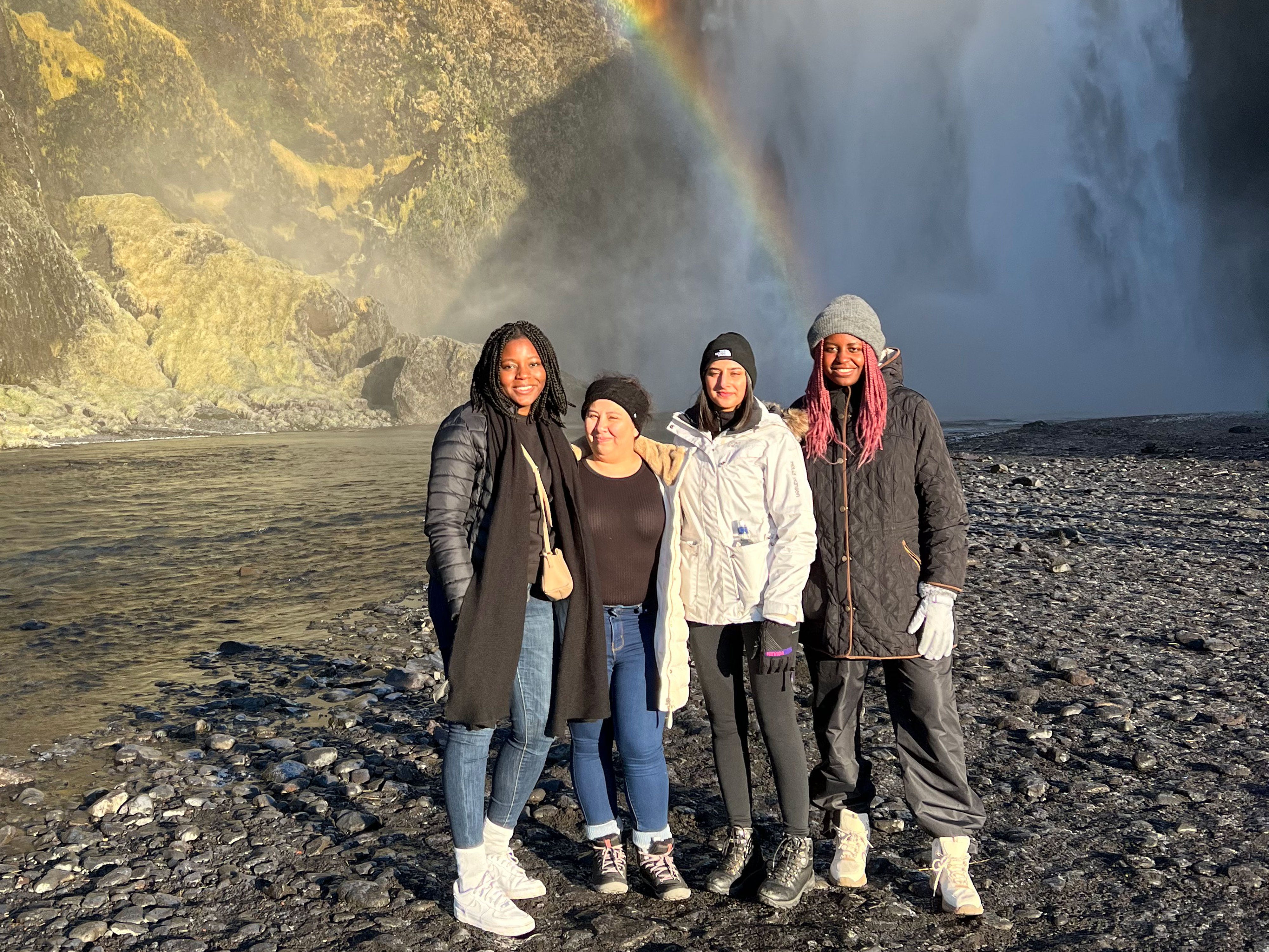 Djena and three friends stand in front of a waterfall with a rainbow.